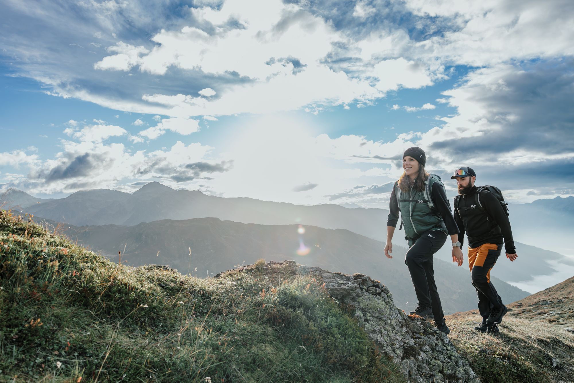 Man en vrouw in Jack Wolfskin outdoor kleding wandelen een berg op tijdens een zonnige dag.