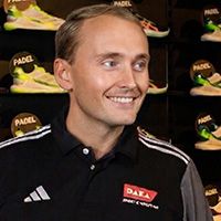 Pepijn Man in a black Adidas polo shirt stands smiling in front of a display of athletic shoes labeled "PADEL" in the background.