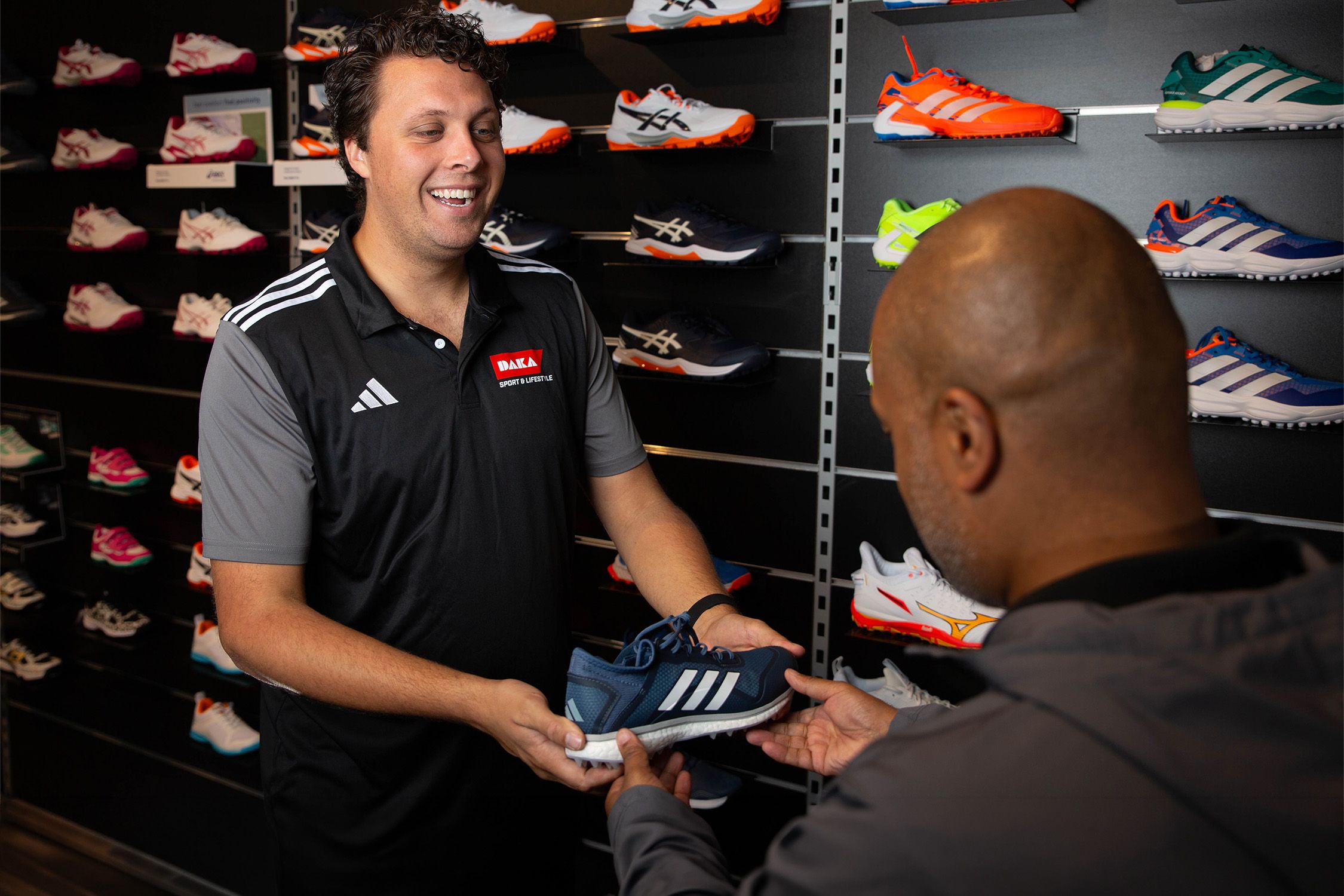 Verkoper met een man in een sportwinkel voor een wand hockeyschoenen