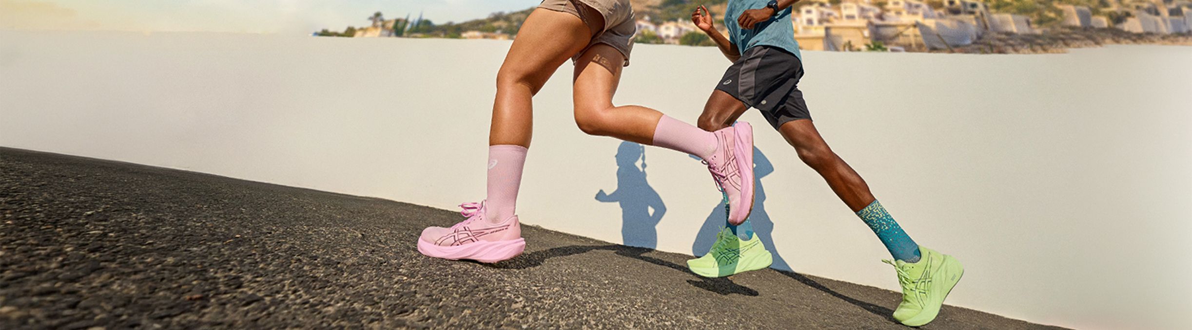 Two people running on a hill, wearing colorful sneakers; one in pink shoes and socks, the other in green shoes and blue socks, against a sunny backdrop.