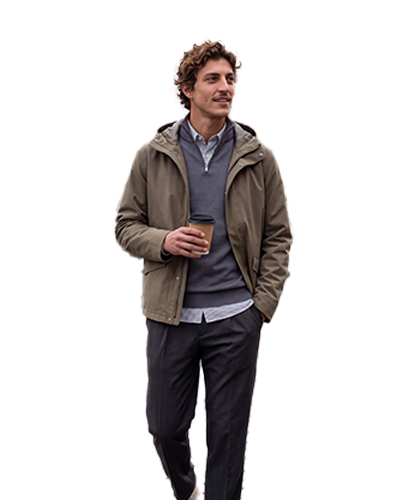 Heren Man in a jacket holding a coffee cup walks on a cobblestone path by colorful buildings and a canal.