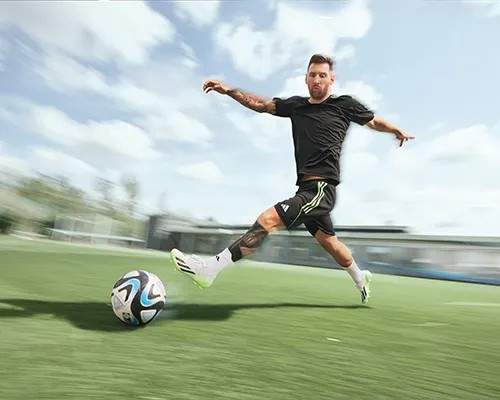 Goed voorbereid het voetbalseizoen beginnen Soccer player in motion wearing black athletic wear, kicking a ball on a grassy field under a blue sky.