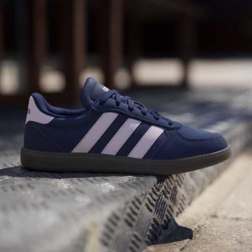 A blue sneaker with white stripes and a logo on the heel, placed outdoors on a textured surface.