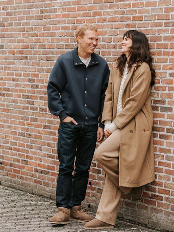 A man and woman stand laughing against a brick wall, both wearing casual winter clothing and Warmbat boots.