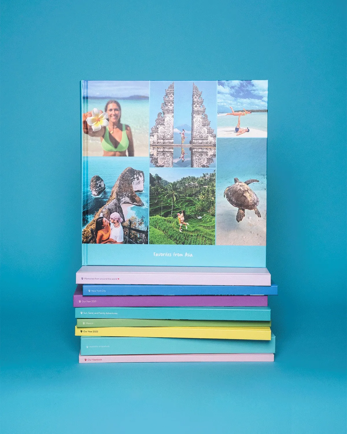 A stack of colorful hardcover photo books with the top book featuring travel photos, including beaches, temples, and wildlife, against a blue background.