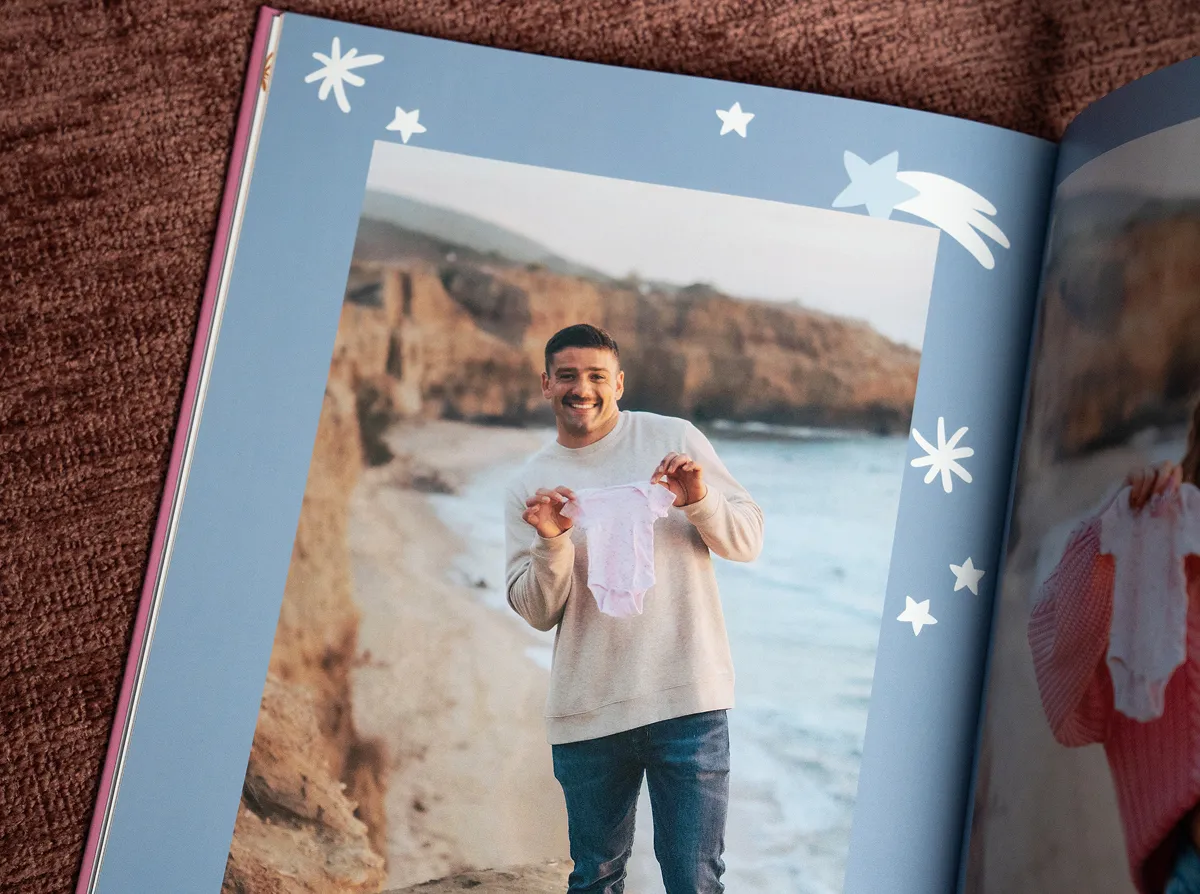 A photo book featuring a man happily holding a small piece of baby clothing on a beach with star and shooting star decorations.