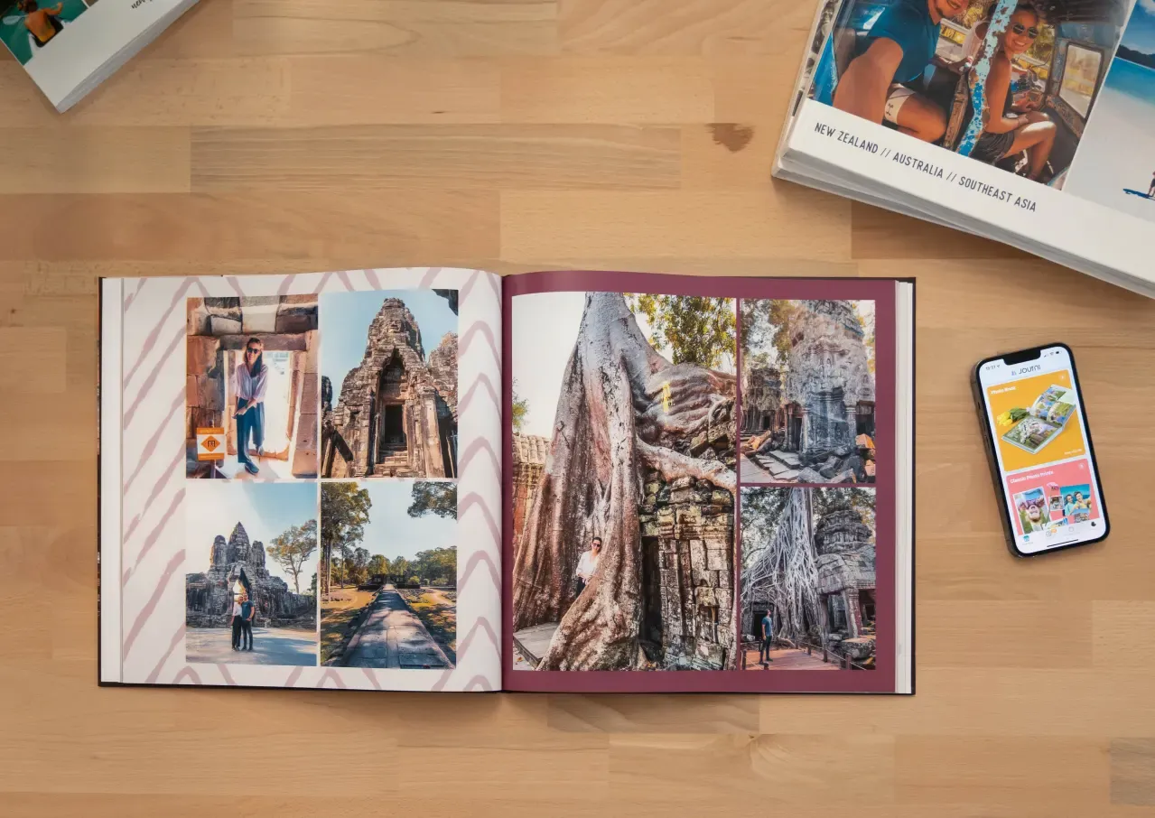 Open photo book displaying travel images, placed on a wooden table next to a phone and a book titled "New Zealand / Australia / Southeast Asia."