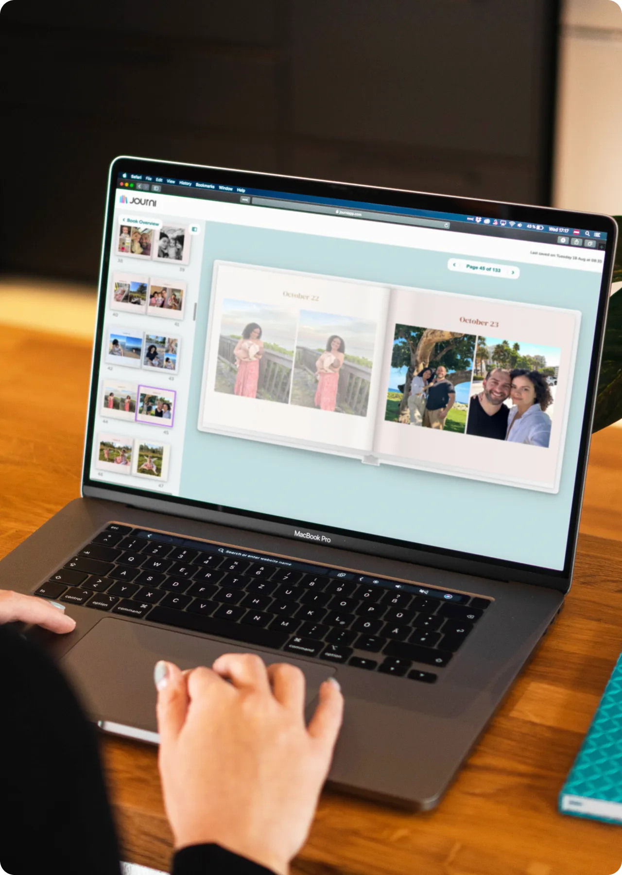 A person using a MacBook Pro to view a photo album on a digital platform, with images dated October 22 and 23 displayed.