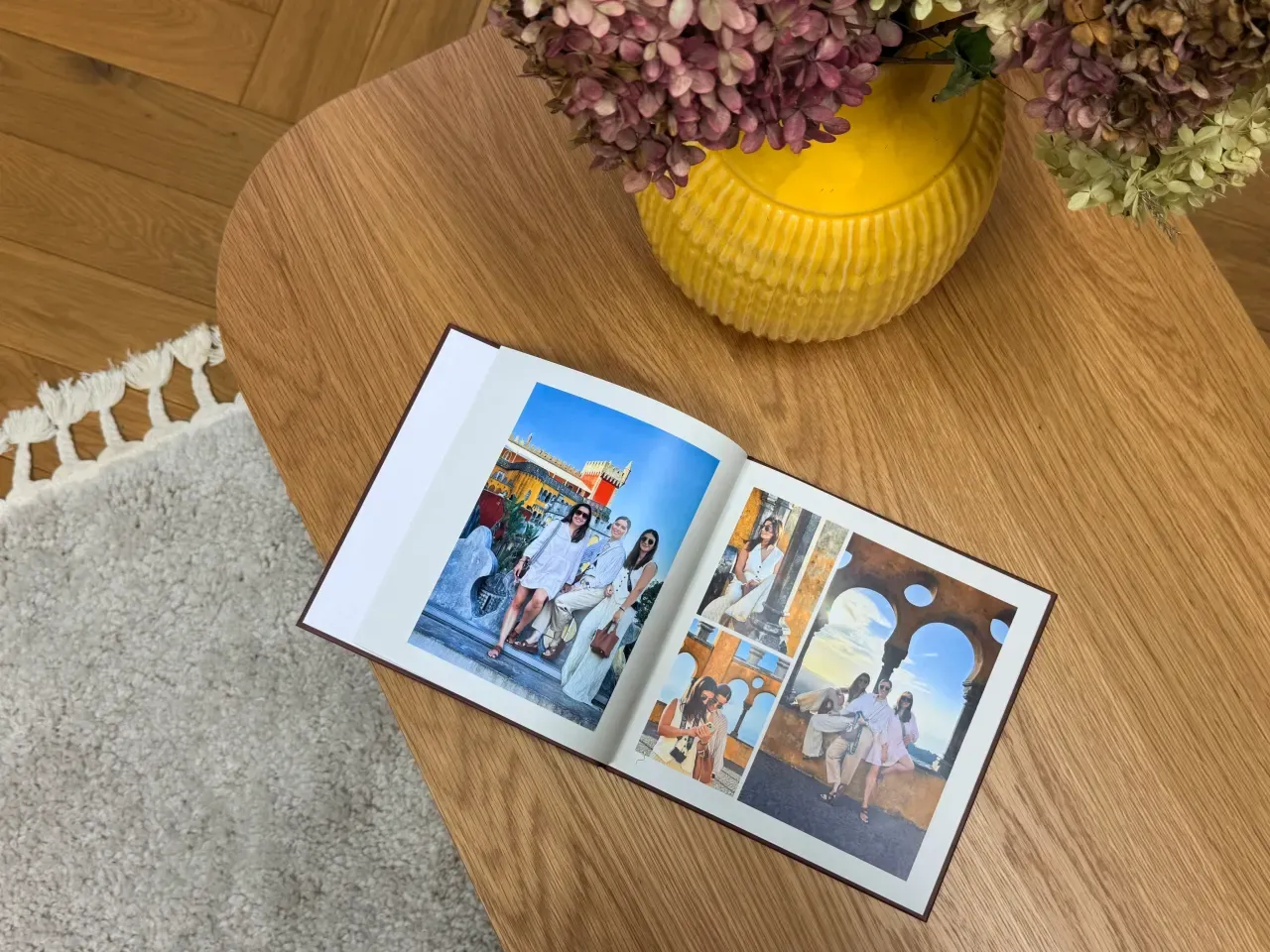 An open premium travel photo book displayed on a wooden table, showcasing vibrant, high-vibrancy travel photography layouts next to a bright yellow ceramic vase filled with fresh hydrangeas.