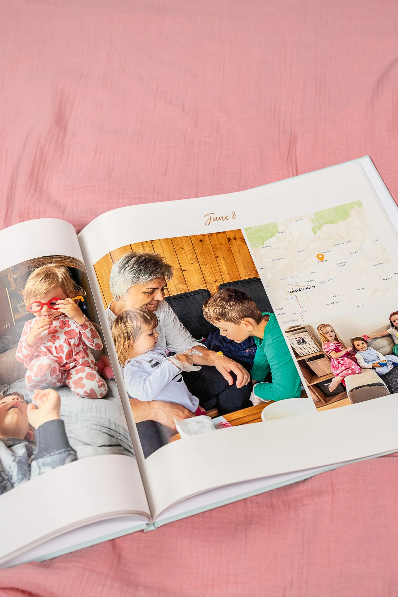 Ein offenes Fotobuch auf rosa Stoff, in dem Familienfotos und eine Karte zu sehen sind; oben steht das Datum „8. Juni“.