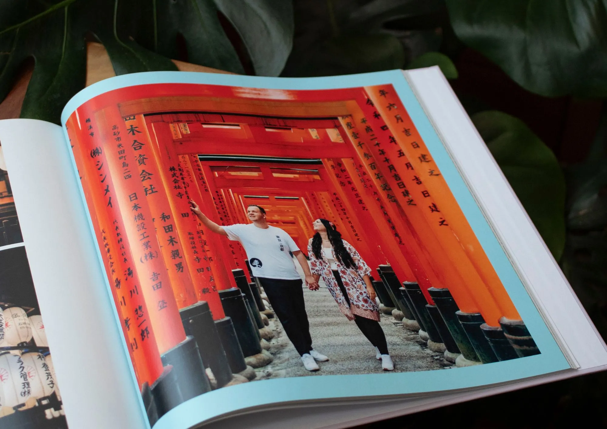 A couple walks through vibrant red torii gates in Japan, surrounded by lush greenery, captured in a photo book.