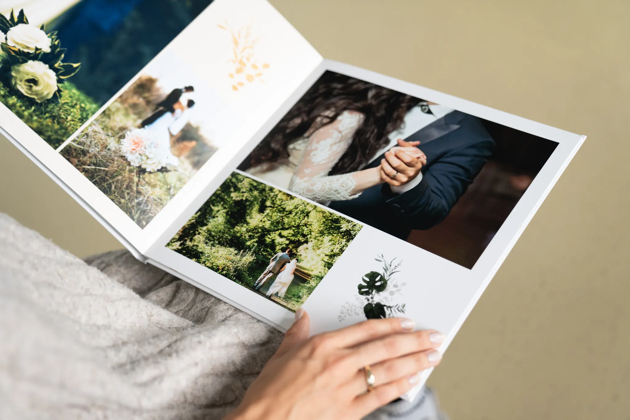 Person holding an open wedding photo album with images of a couple, nature scenes, and floral designs on a light background.