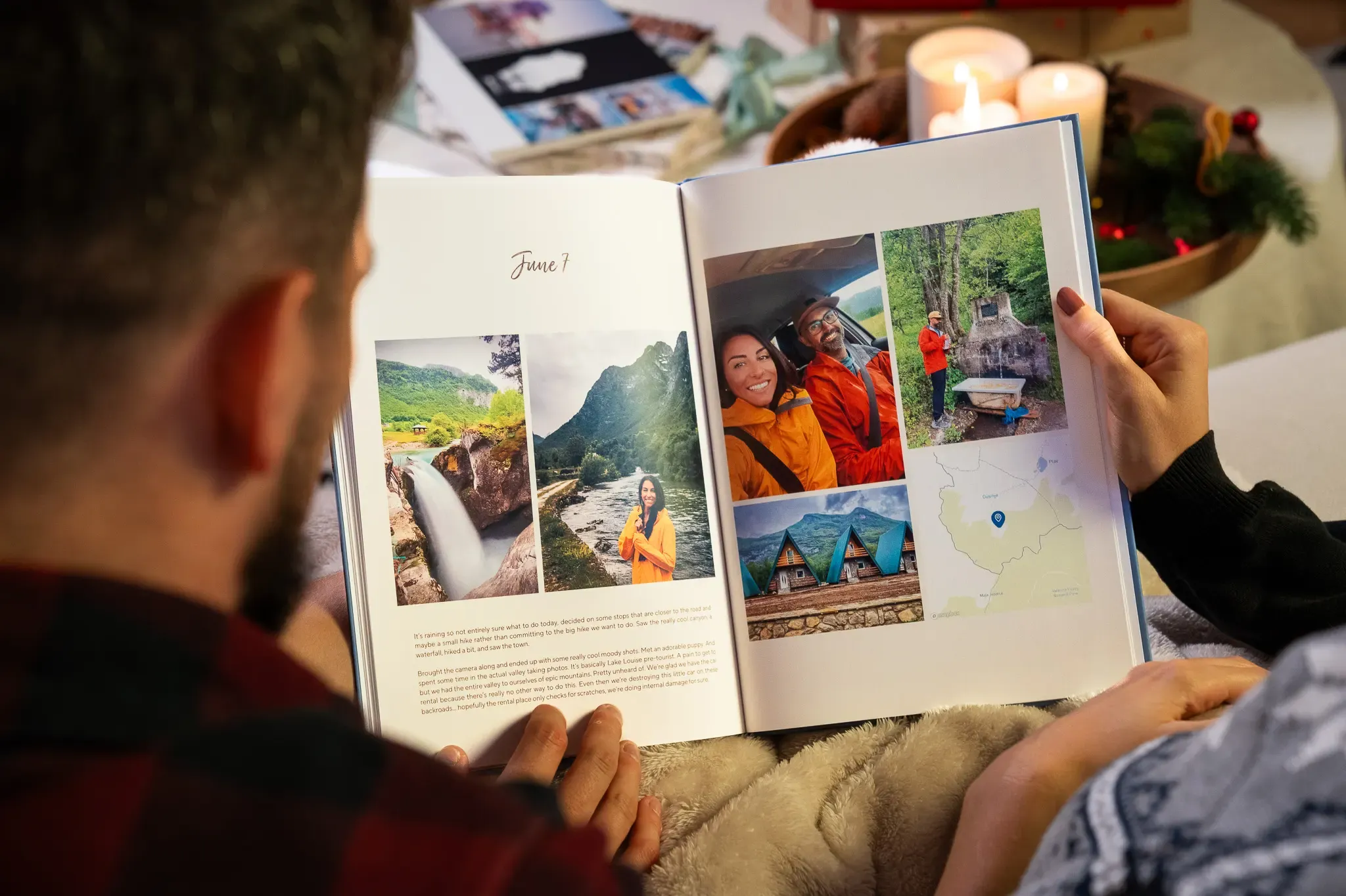 A couple looks at a photo album showing scenic travel pictures and memories, with candles and holiday decorations in the background.