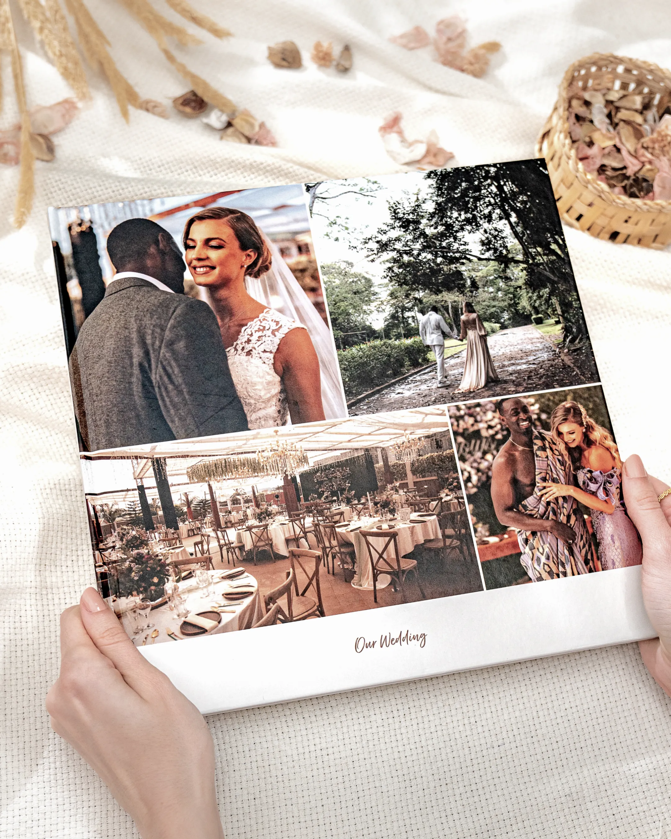 Hands holding a wedding photo album with images of a couple, outdoor ceremony, reception setup, and guests.