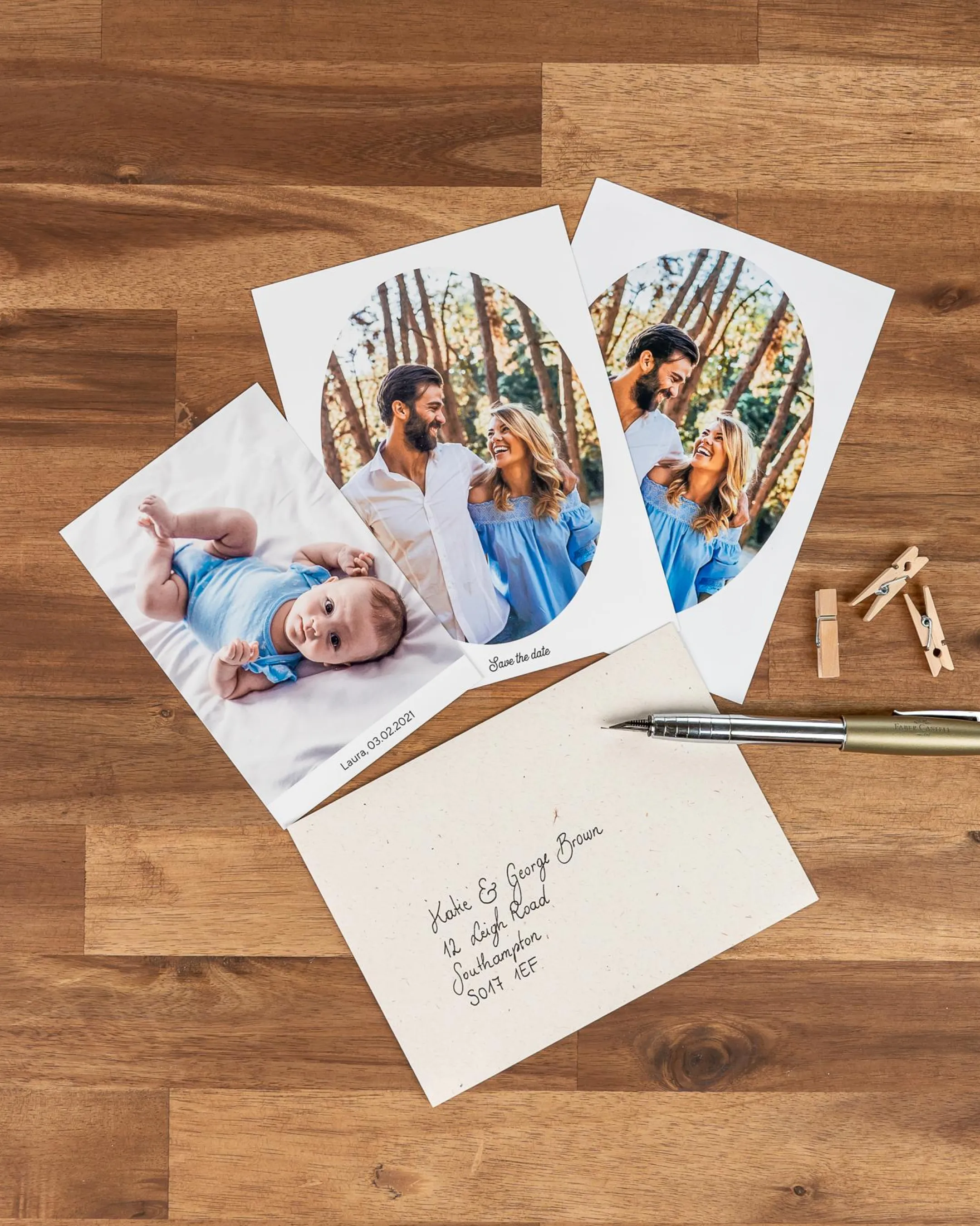 Photos on a wooden table: a baby, a couple outdoors, a pen, mini clothespins, and an envelope with handwritten names and address.