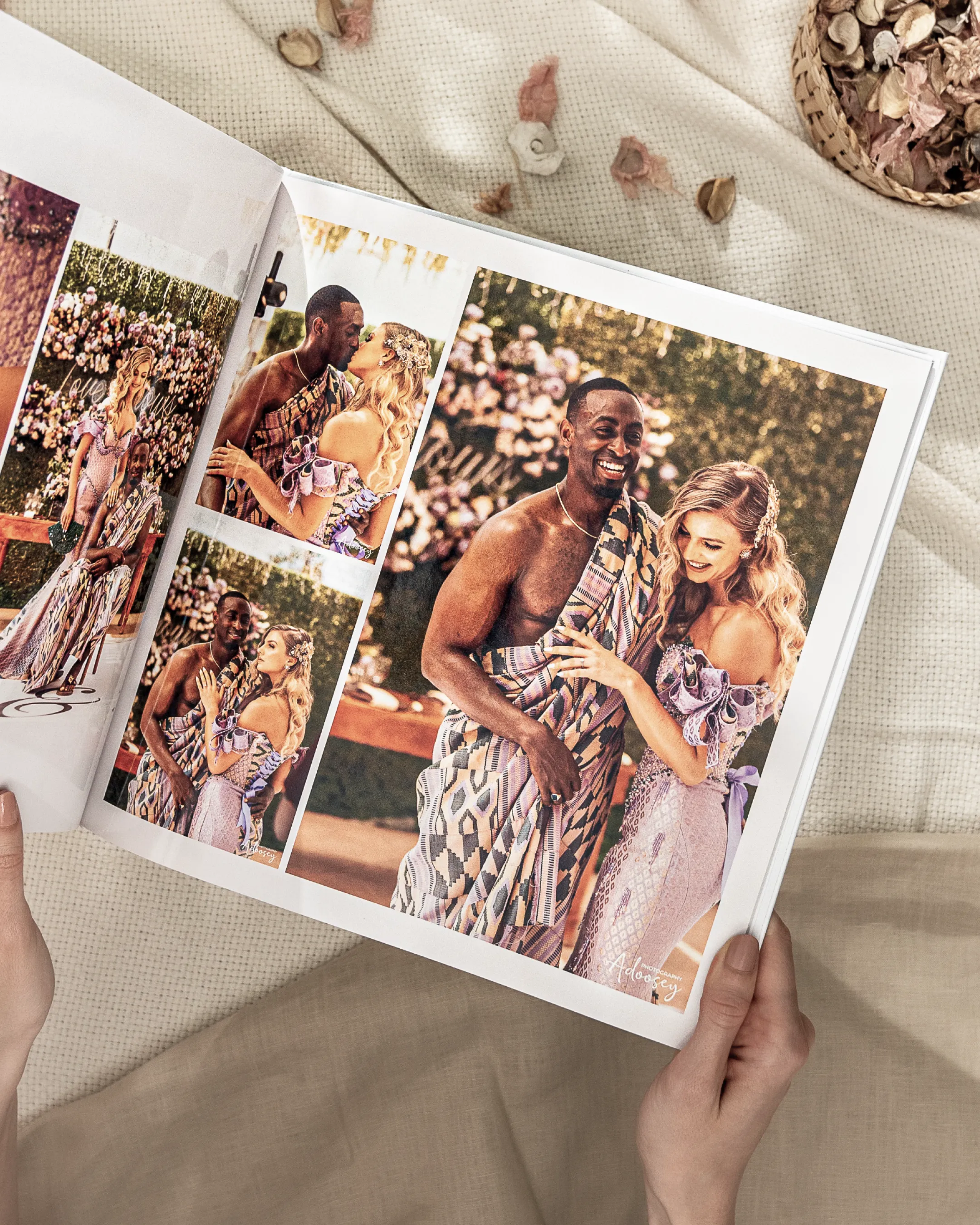 Hands holding a wedding photo album with images of a smiling couple in traditional and formal attire, surrounded by flowers.