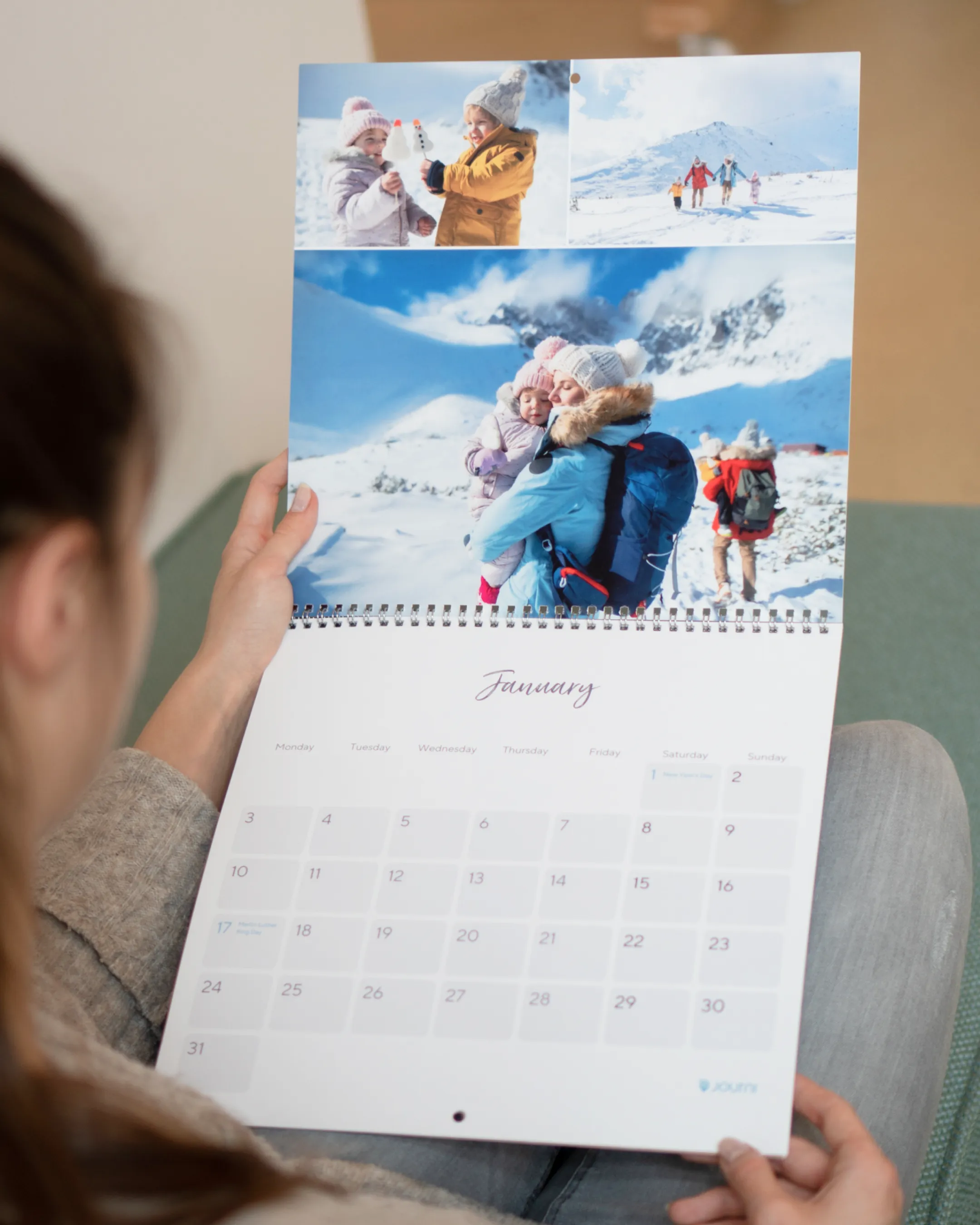 Person holding an open calendar to January, featuring winter photos of people in snowy landscapes.