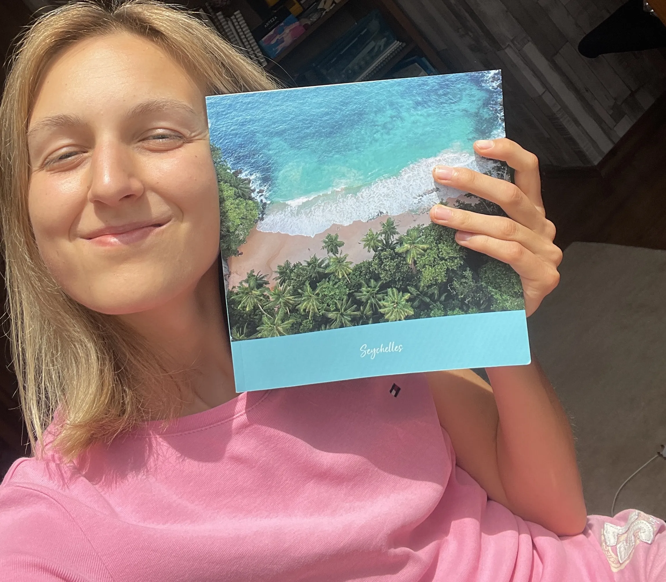 Smiling person holding a book titled "Seychelles" with a cover image of a tropical beach and forest.