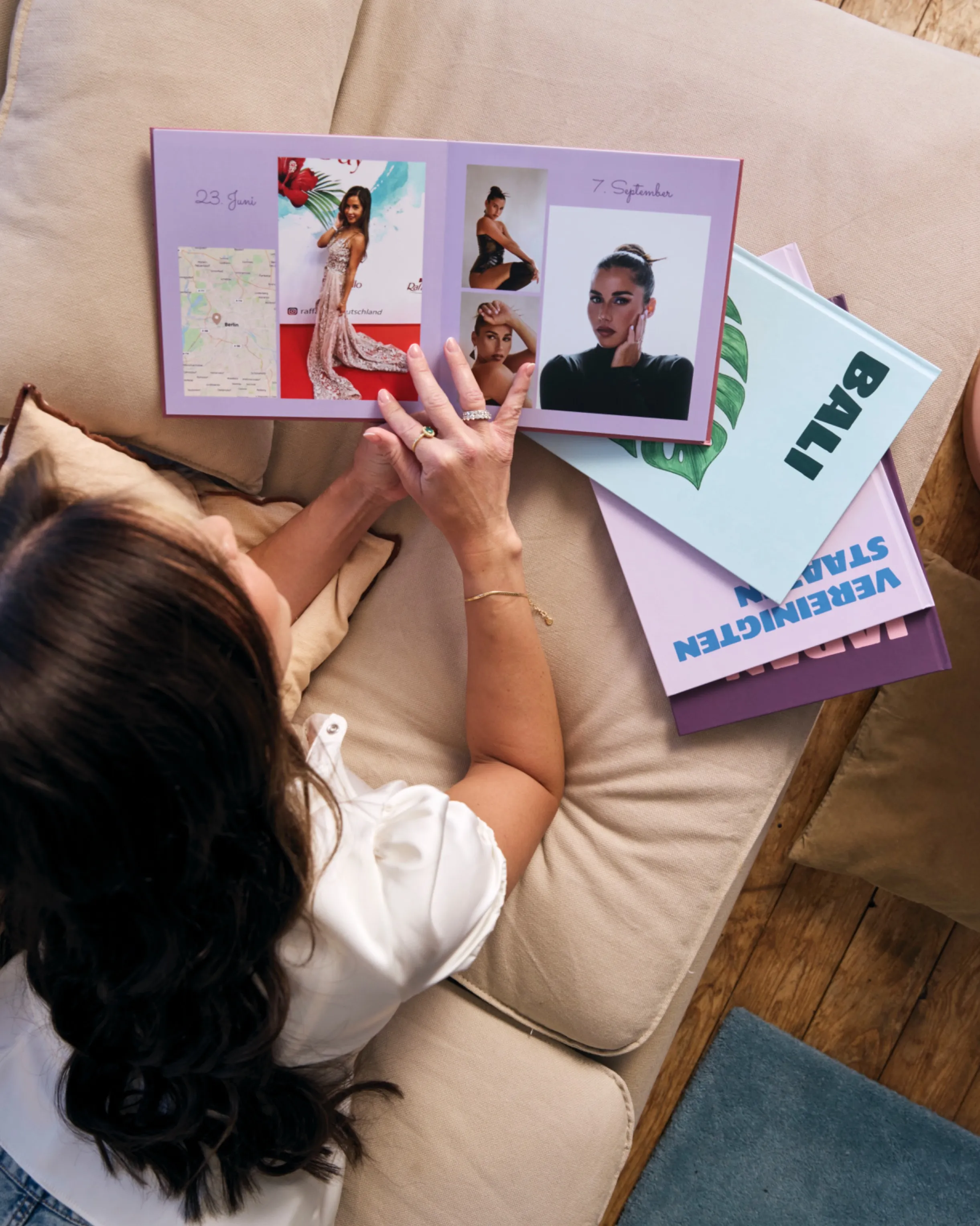 Sara Engels looking through a photo book with images and maps, sitting on a beige couch beside a book titled "BALI".