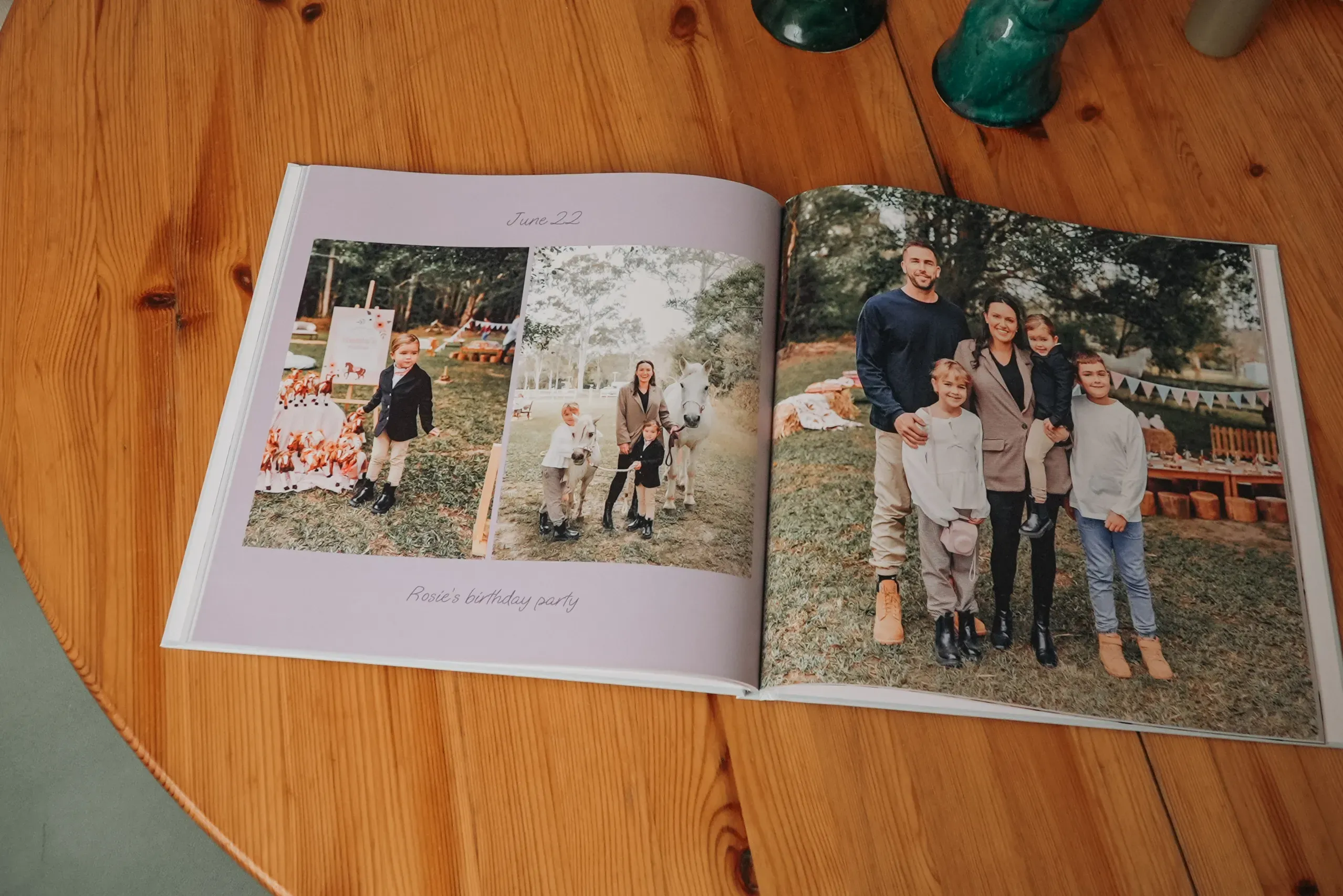 Open photo album on a wooden table showing a family posing together and a birthday party scene with decorations.