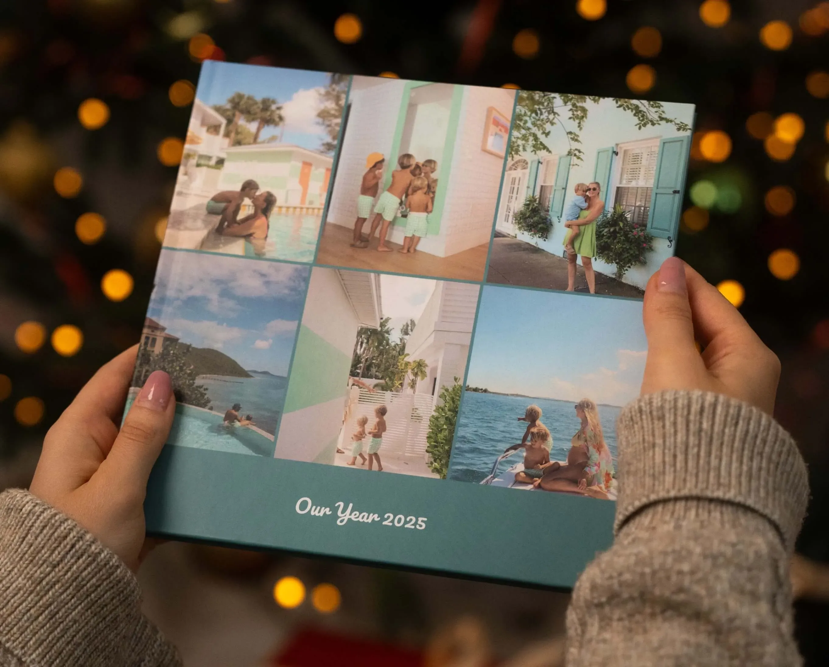 Hands holding a photo book titled "Our Year 2025," featuring vacation photos of a couple by the sea and in tropical settings.