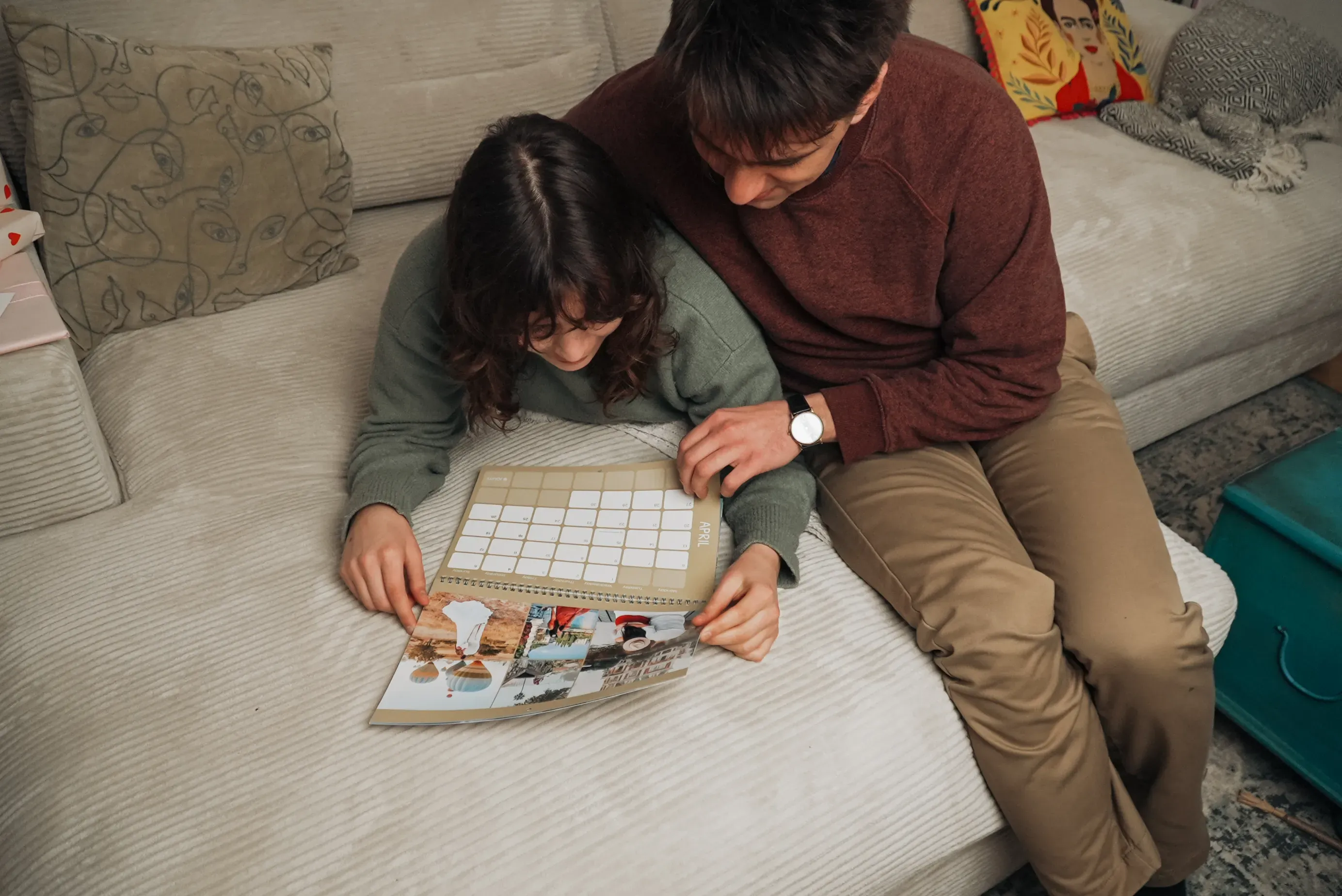 A couple sitting on a couch, looking at a photo calendar together.