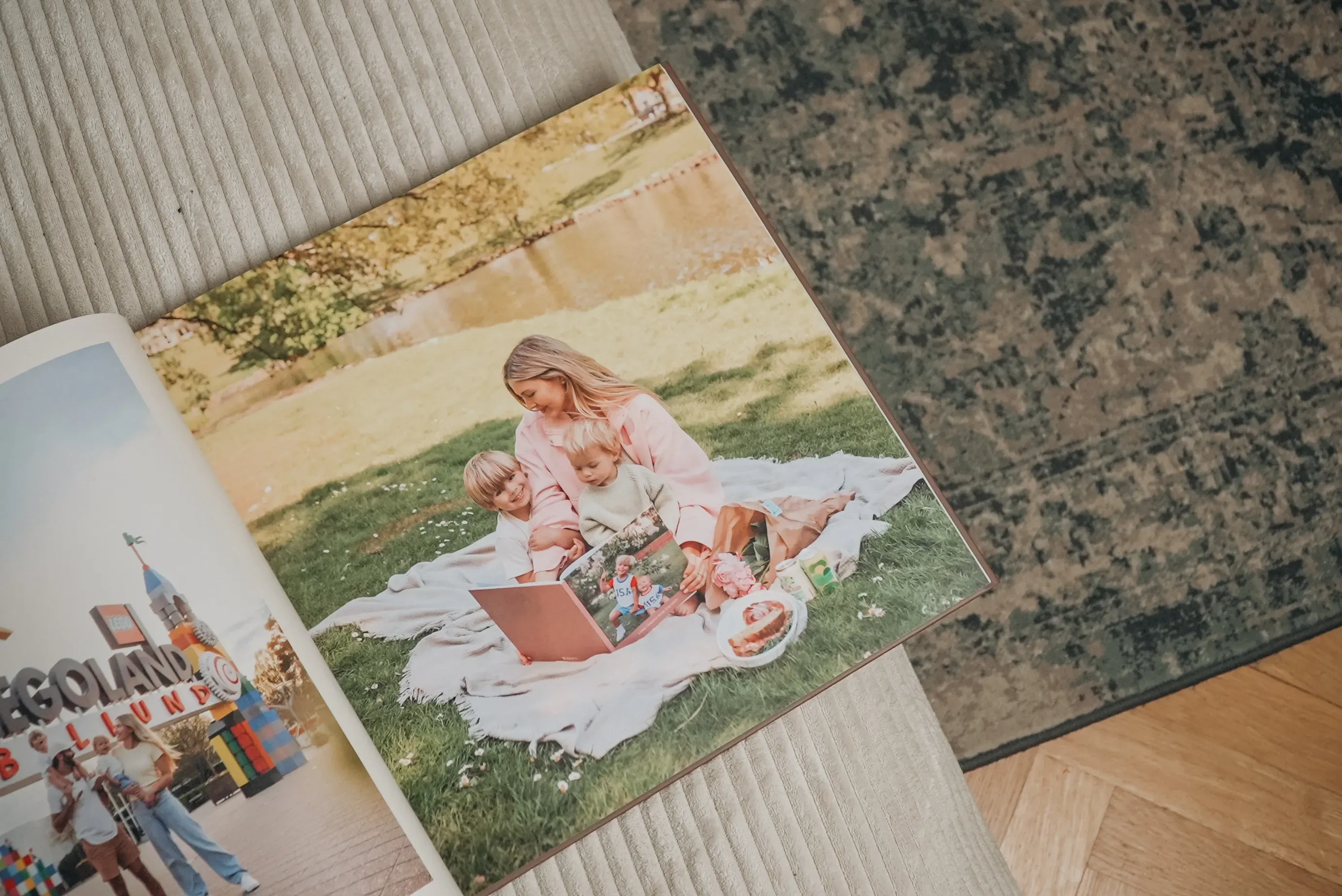 Photo album on table, open to a page showing a woman and two children reading a book on a picnic blanket outdoors. Rug and floor visible beside.