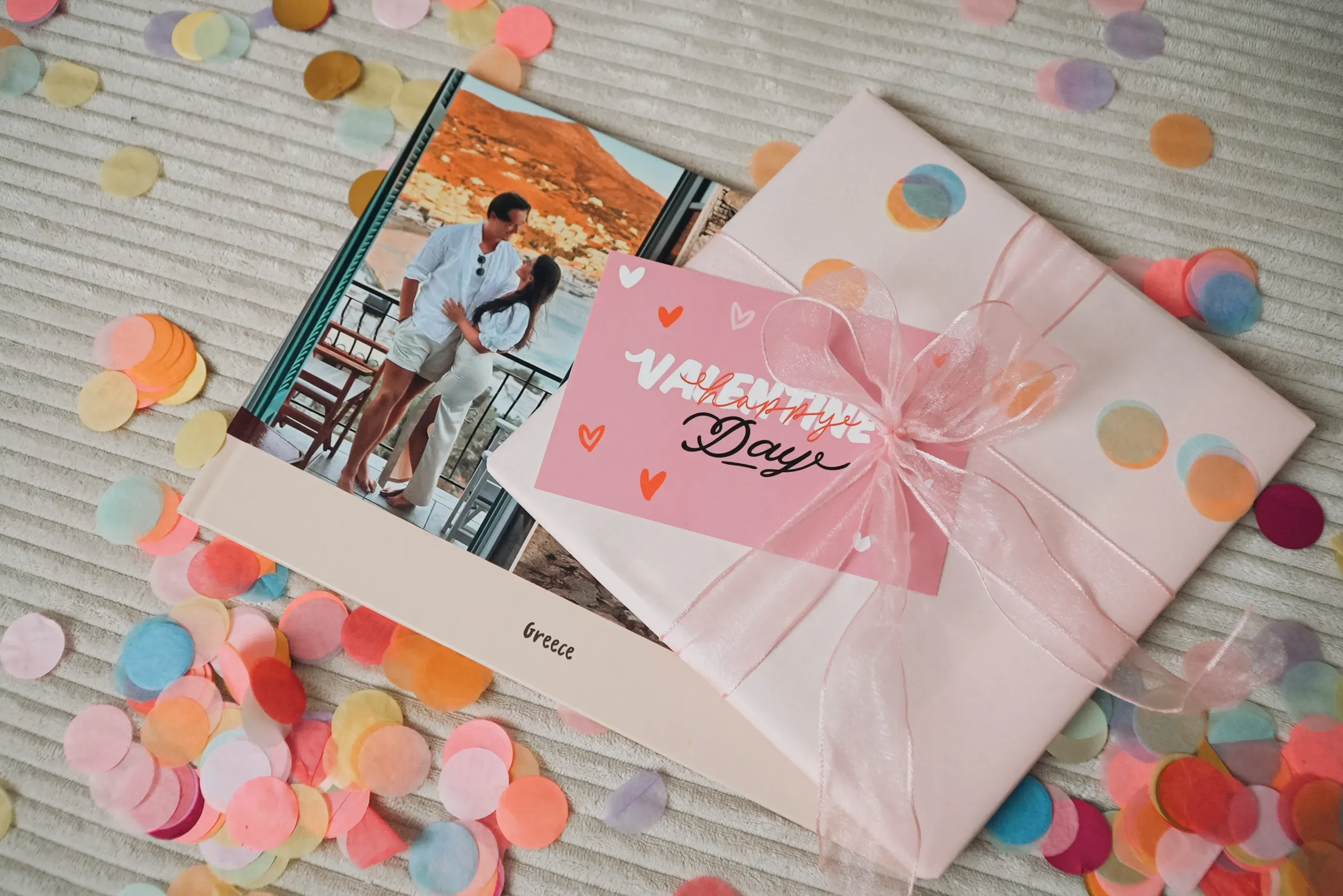 Fotobuch als Valentinstagsgeschenk mit einer Karte und einem Foto eines Paares auf dem Cover, umgeben von buntem Konfetti.