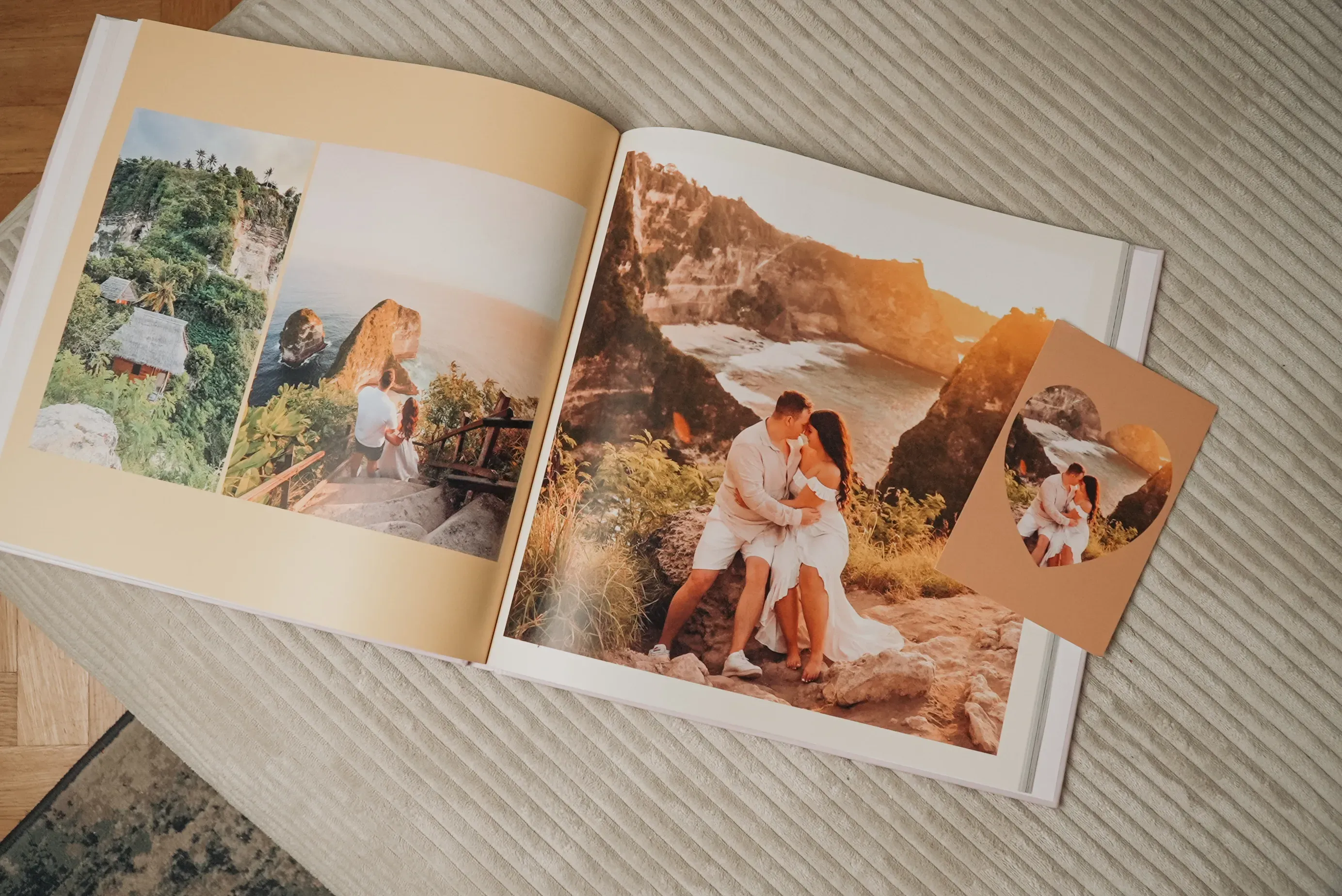 An open photo album on a bed shows a couple embracing on a cliffside, with a small photo featuring the same scene placed nearby.