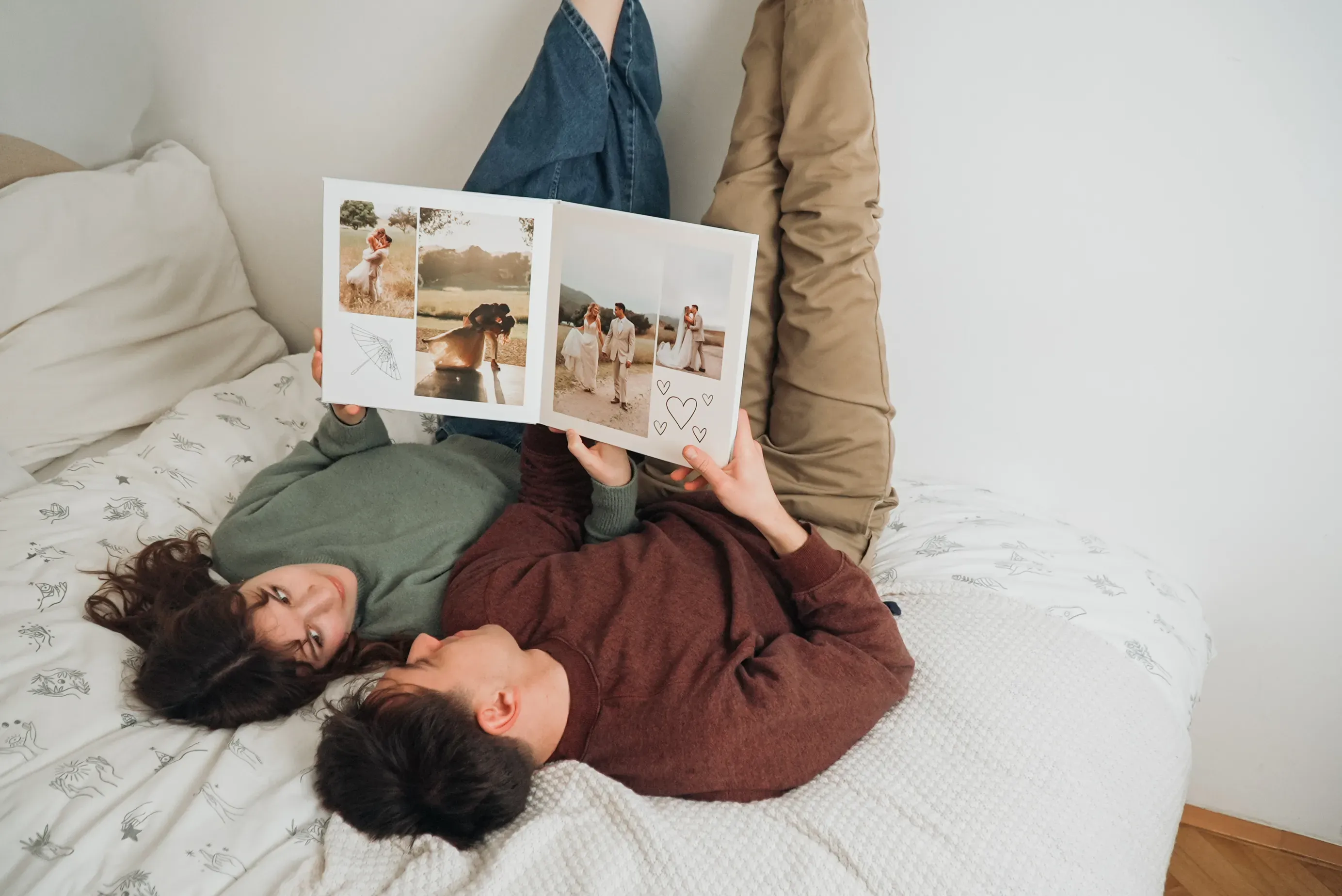 Ein Paar liegt auf einem Bett, die Füße an die Wand gelehnt, und schaut sich ein Fotobuch mit Hochzeitsbildern an.