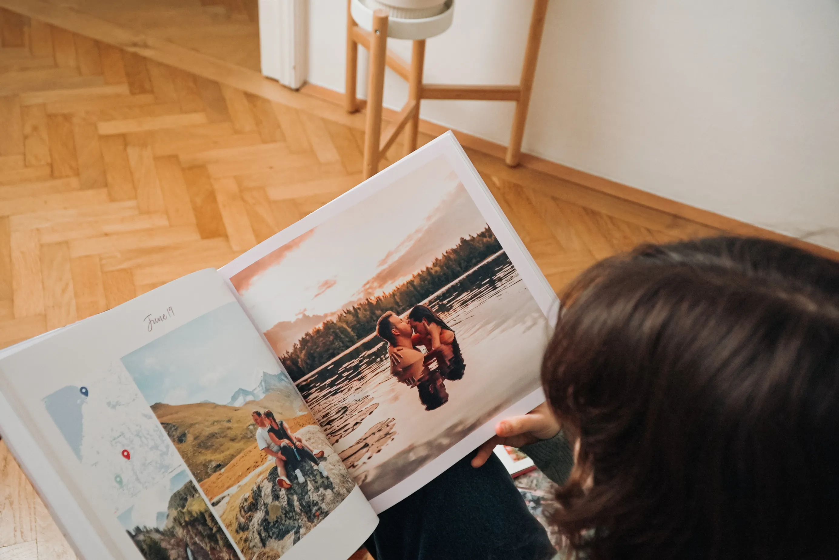 A person is holding and looking at a photo book open to images of scenic landscapes and a couple embracing by a lake.