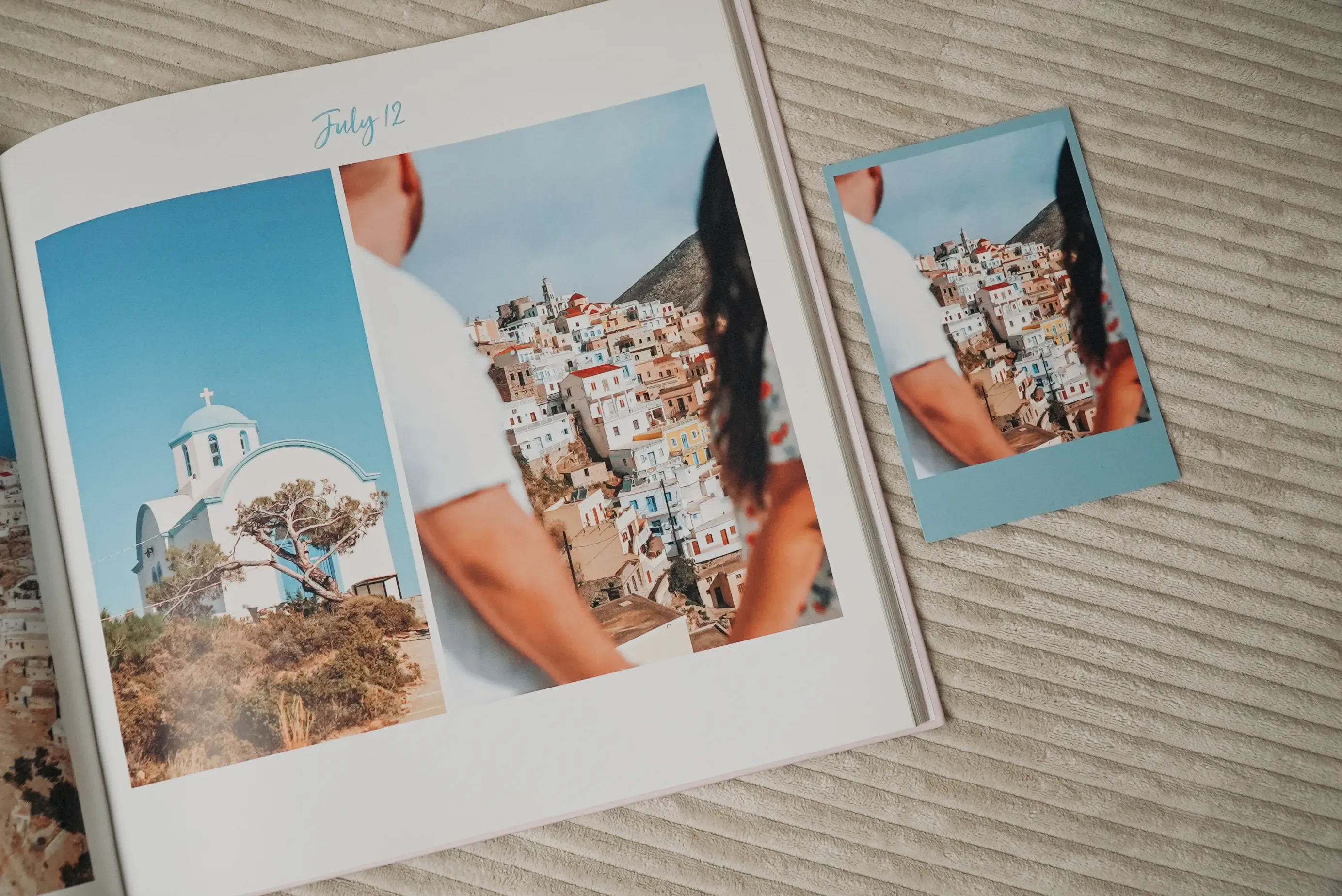 Open photo book and polaroid showing a couple facing a picturesque hillside town with white and blue buildings, dated July 12.