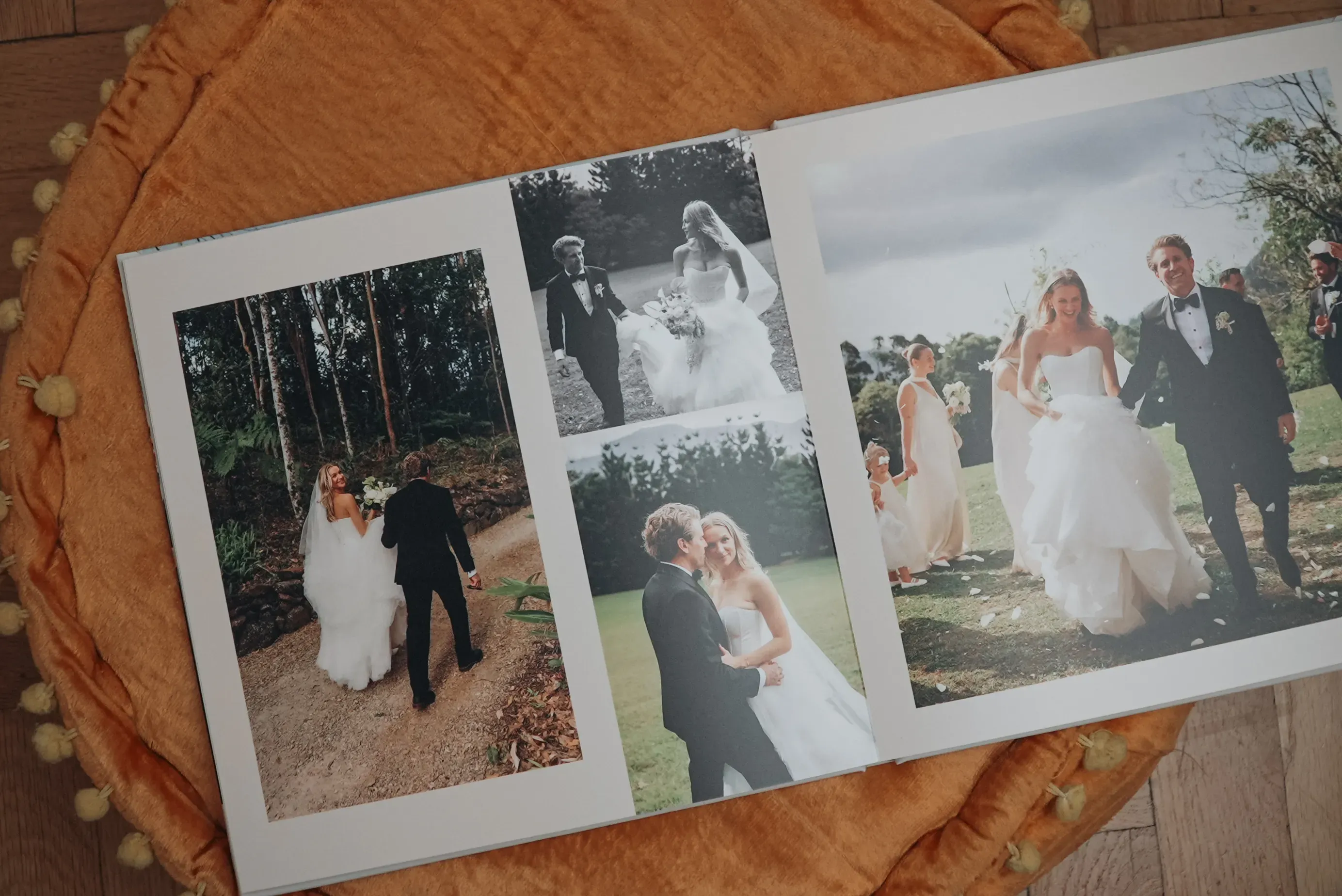 Wedding photo album open to pages with outdoor ceremony images of a couple in formal attire, on an orange blanket background.