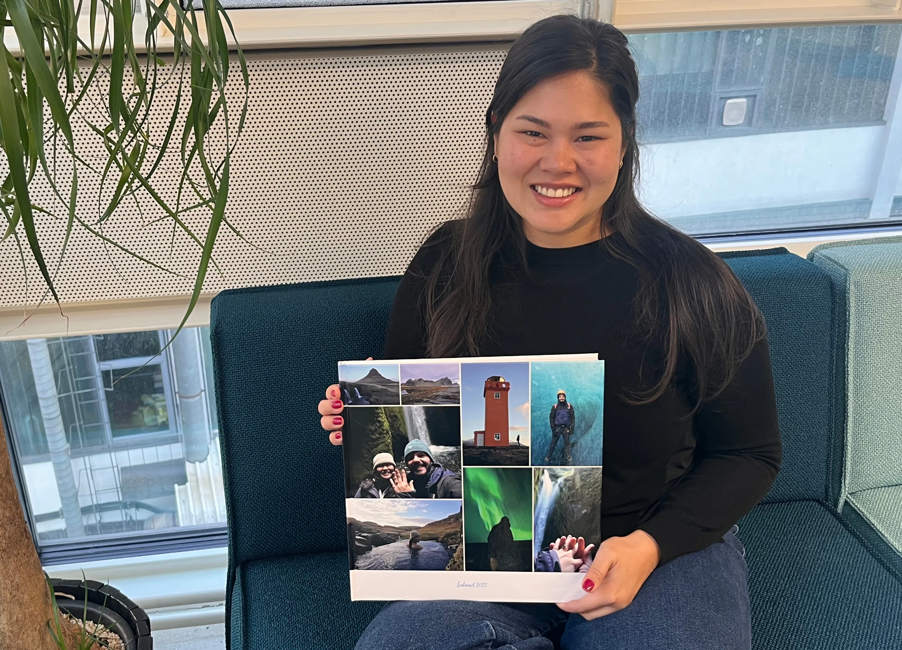 Smiling woman sitting on a couch, holding a photo collage featuring travel scenes, including landscapes and the Northern Lights.