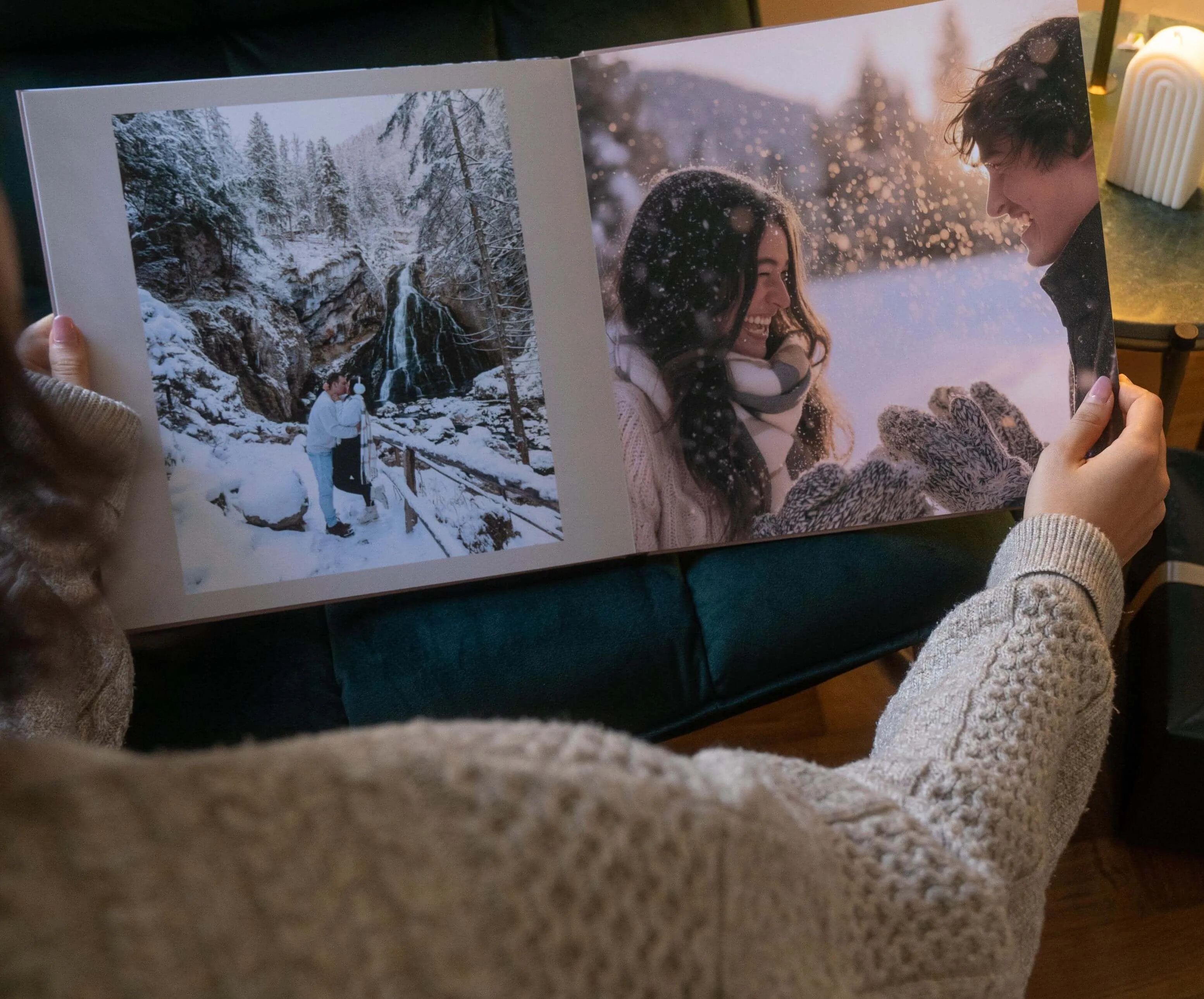 Person holding a photo album featuring snowy scenes with a couple smiling and enjoying a winter landscape.