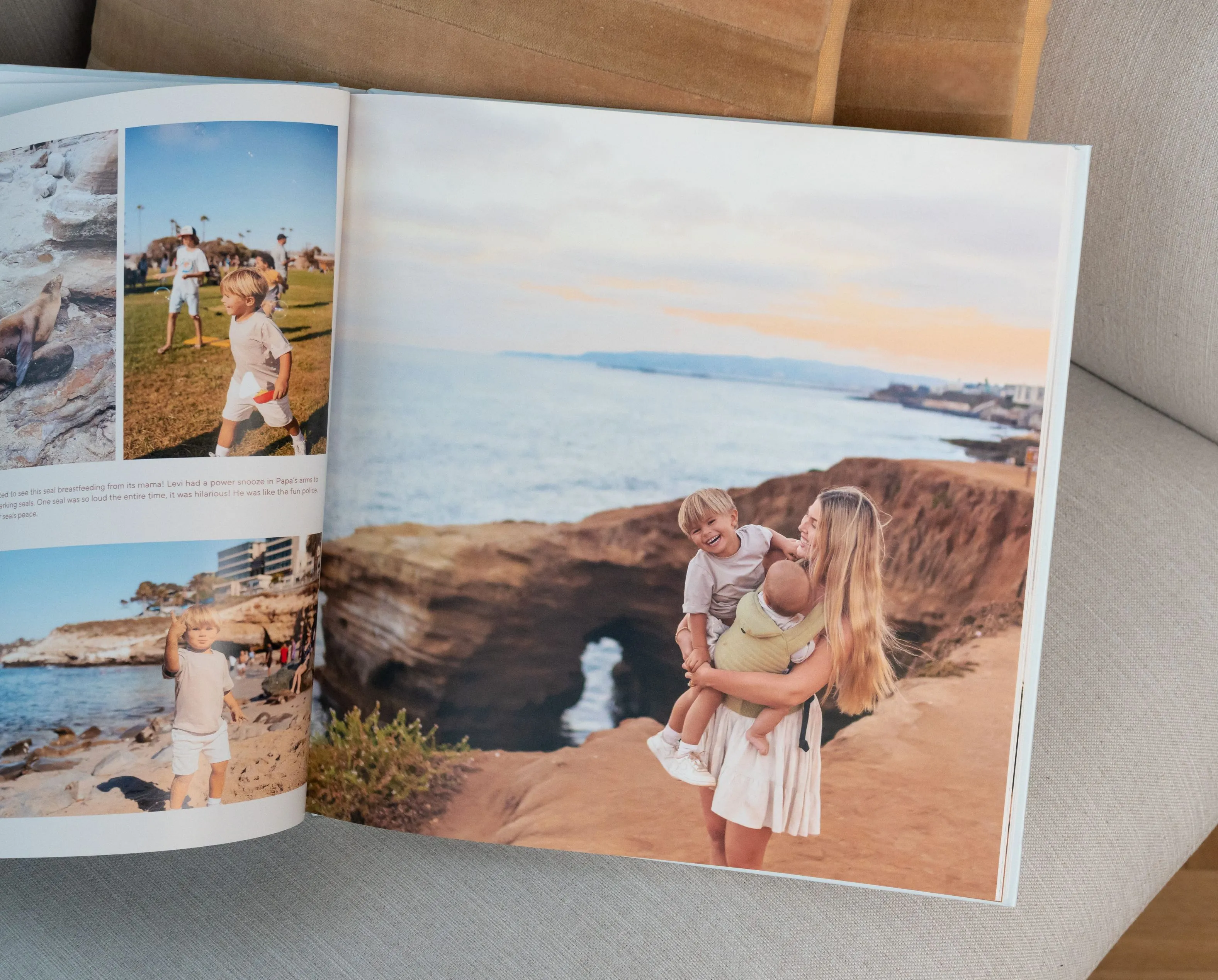 Open photo album on a couch showing a woman holding a child by a rocky coastline with the ocean and sky in the background.