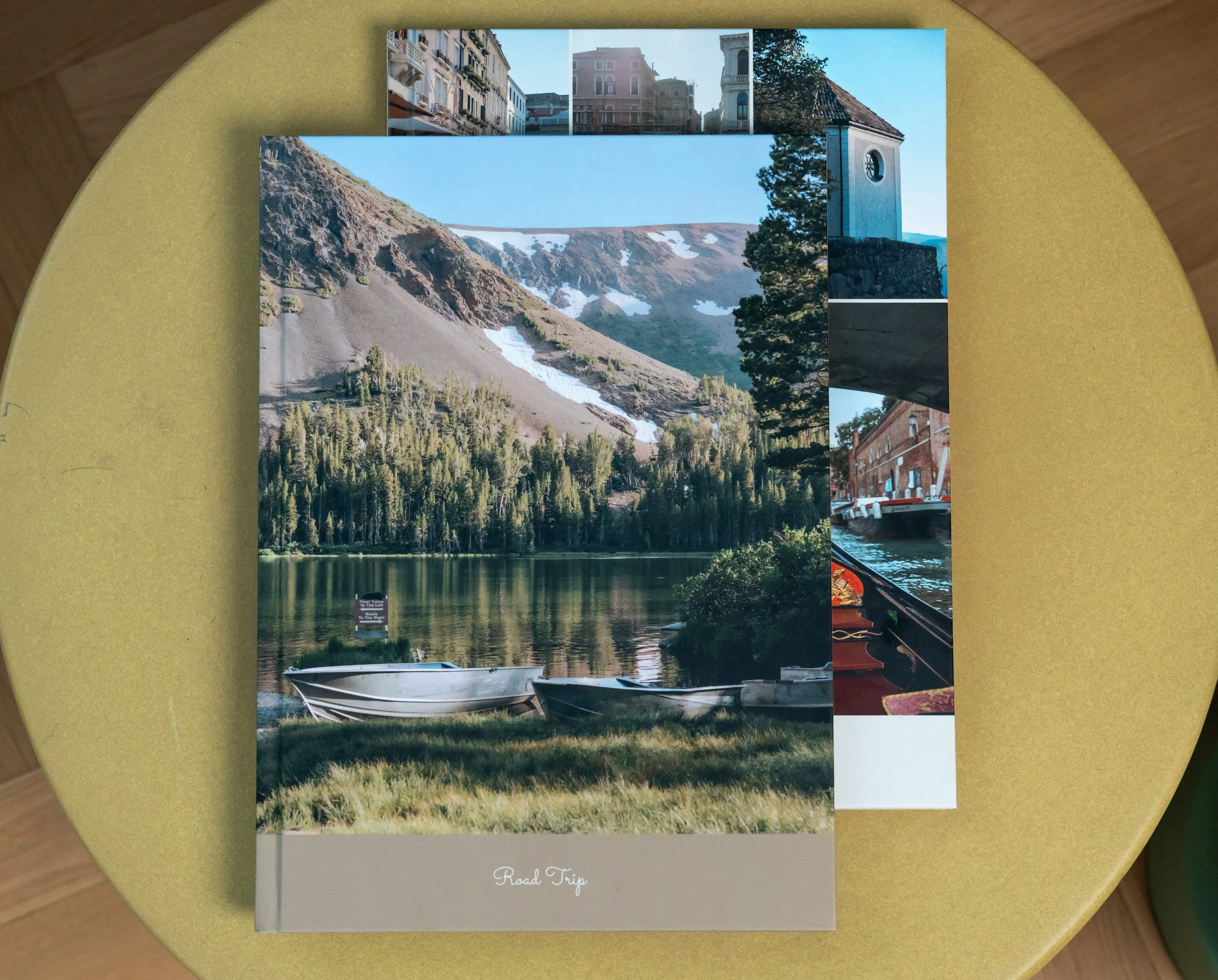 A scenic nature photo book with two inserted travel brochures on a round, green table.