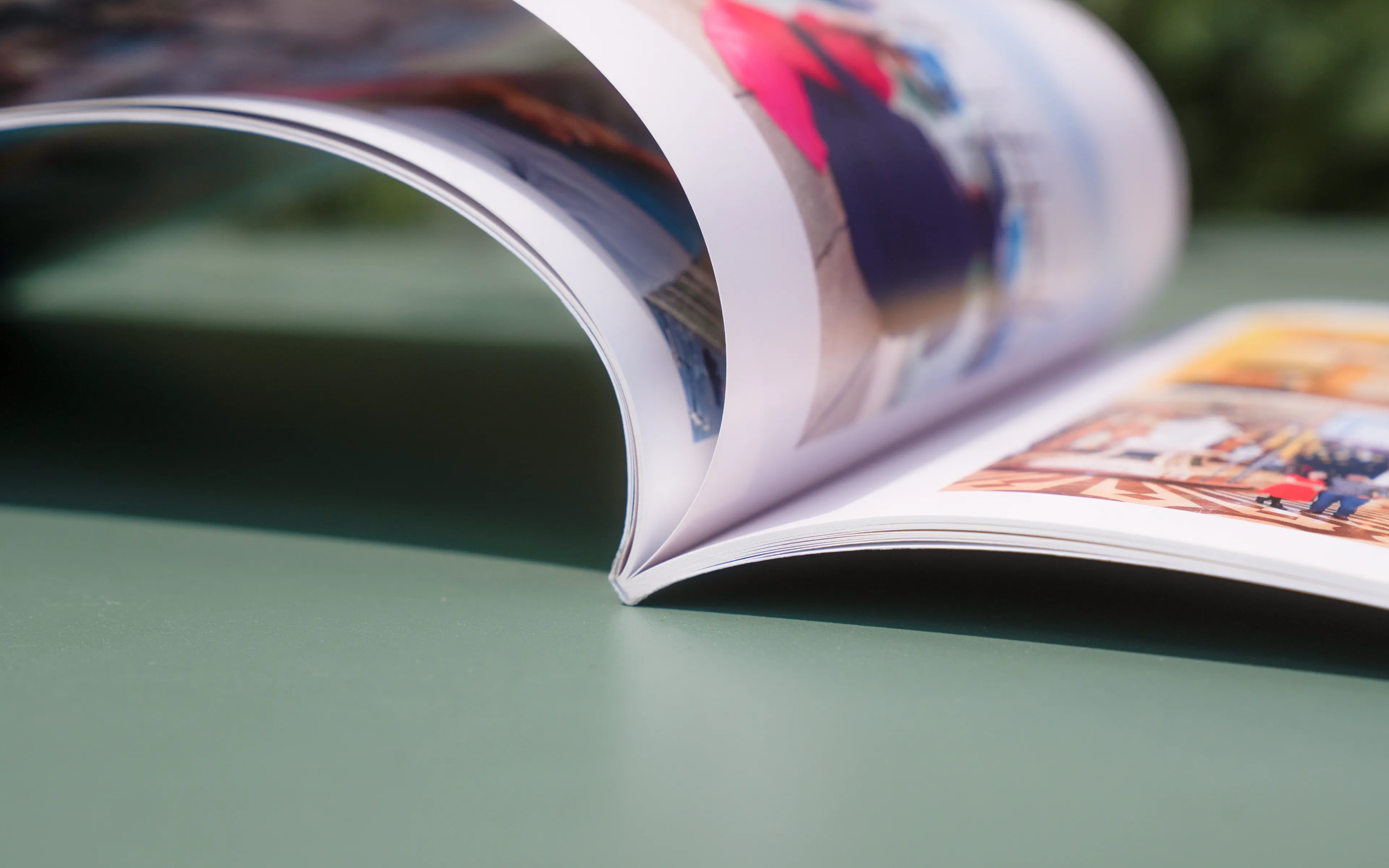 An open photo book on a green surface, showing colorful images on its glossy pages.