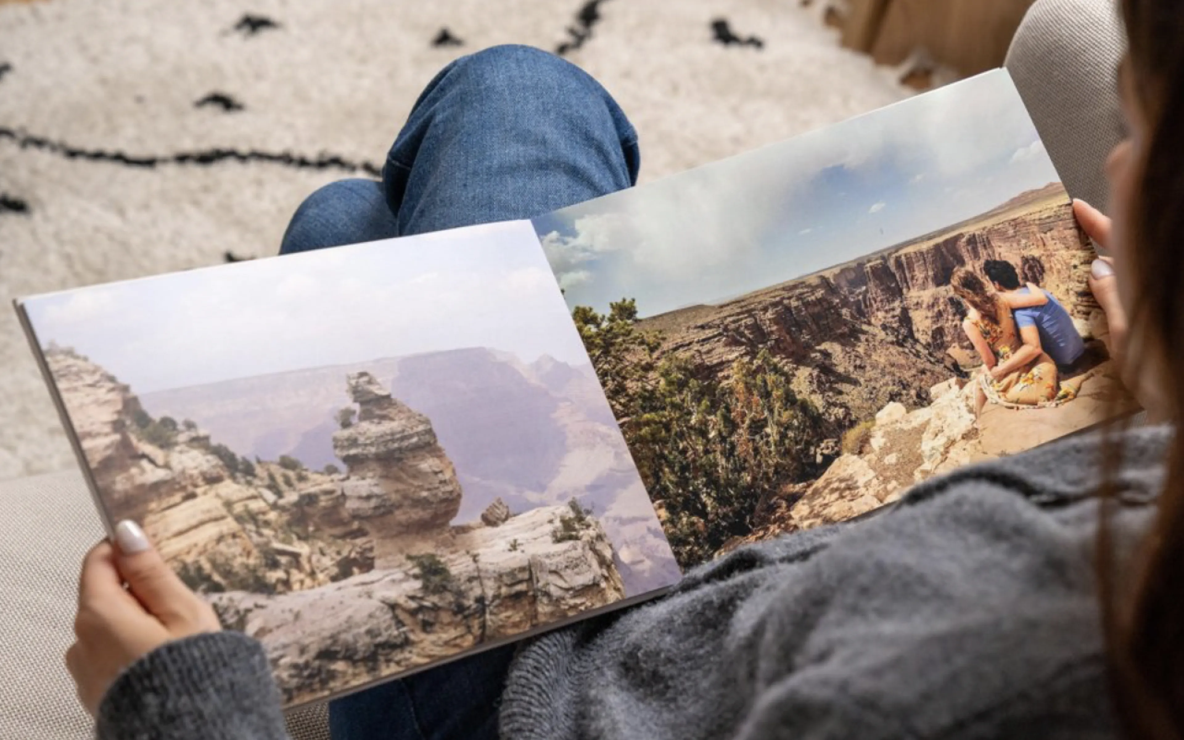 Person holding a photo book open to pages showing scenic canyon landscapes and people sitting on a cliff edge.