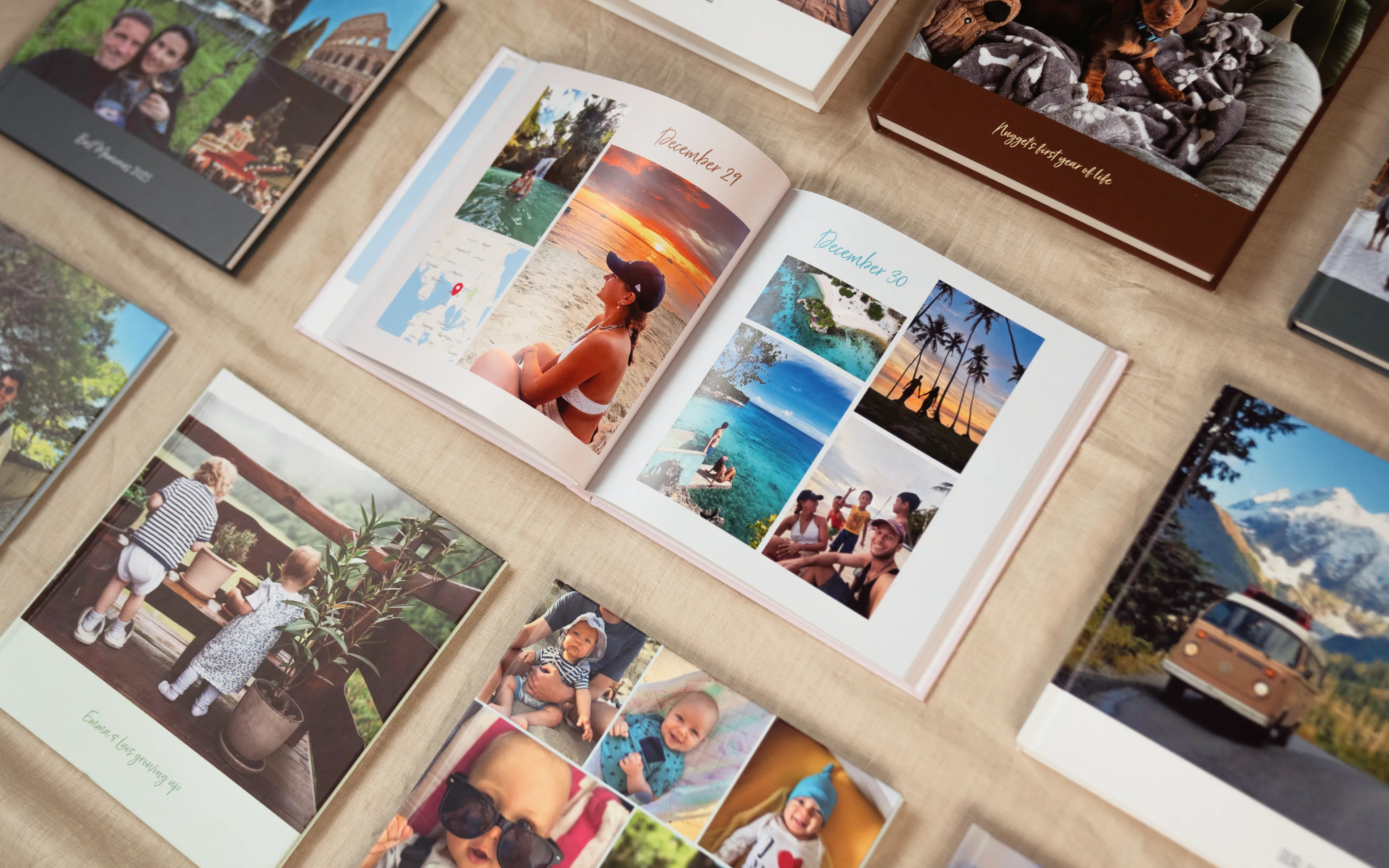 Open photo book with beach and sunset images, surrounded by other albums featuring travel and family photos on a beige surface.