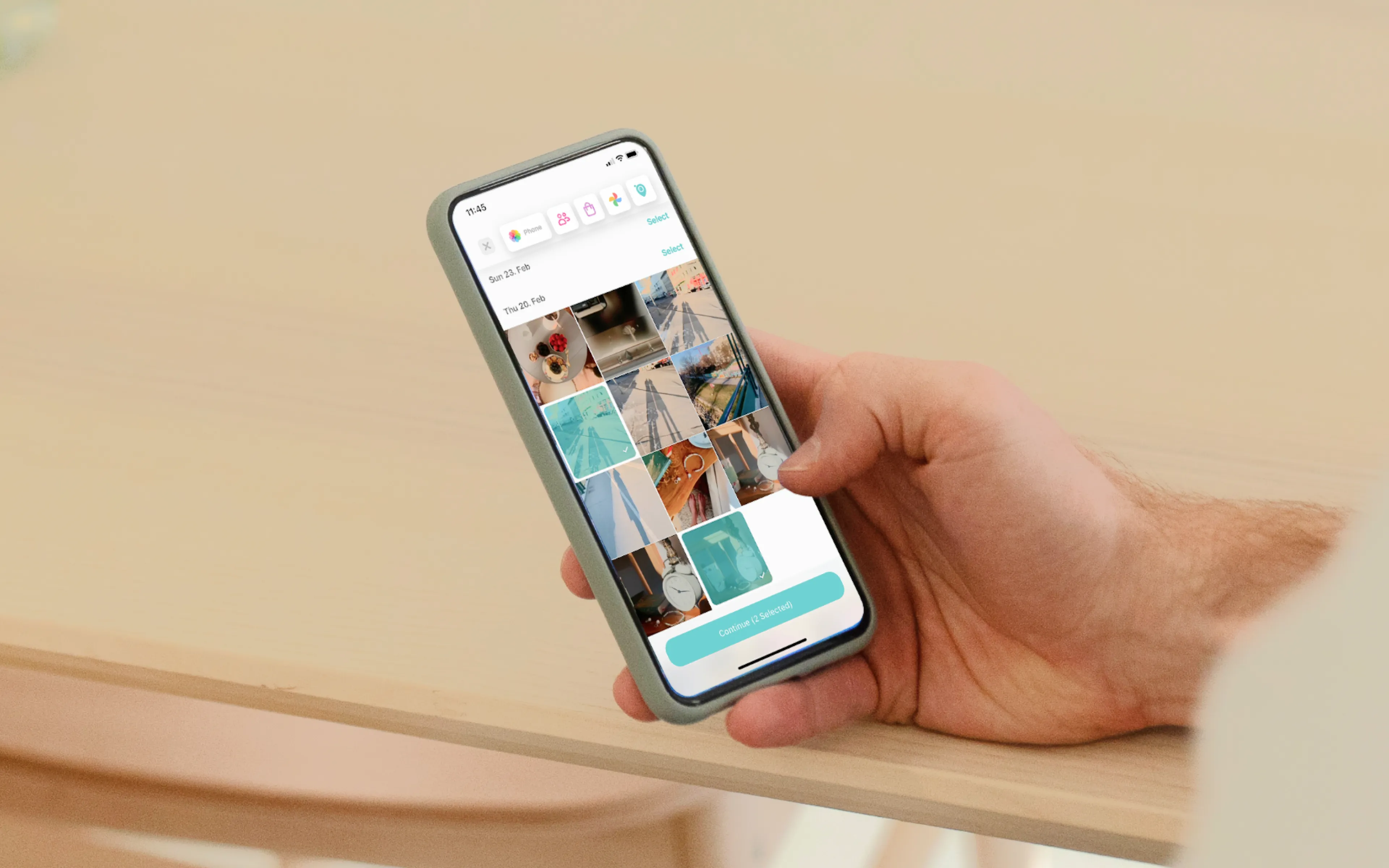 Hand holding a smartphone displaying a gallery of photos on the screen, with a wooden table in the background.