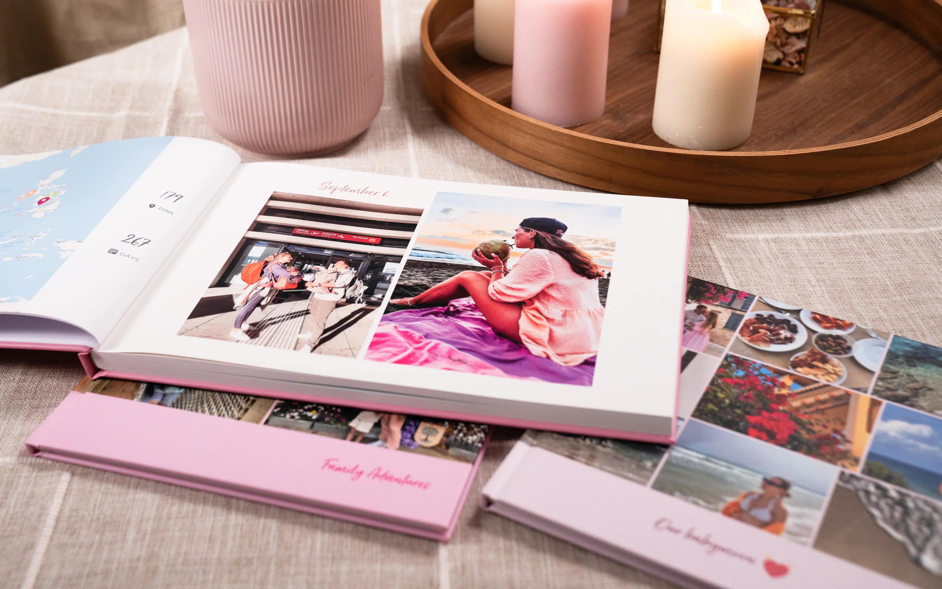 Open photo album on a table with images of a woman and child. Nearby are candles, a pink vase, and more albums with travel photos.