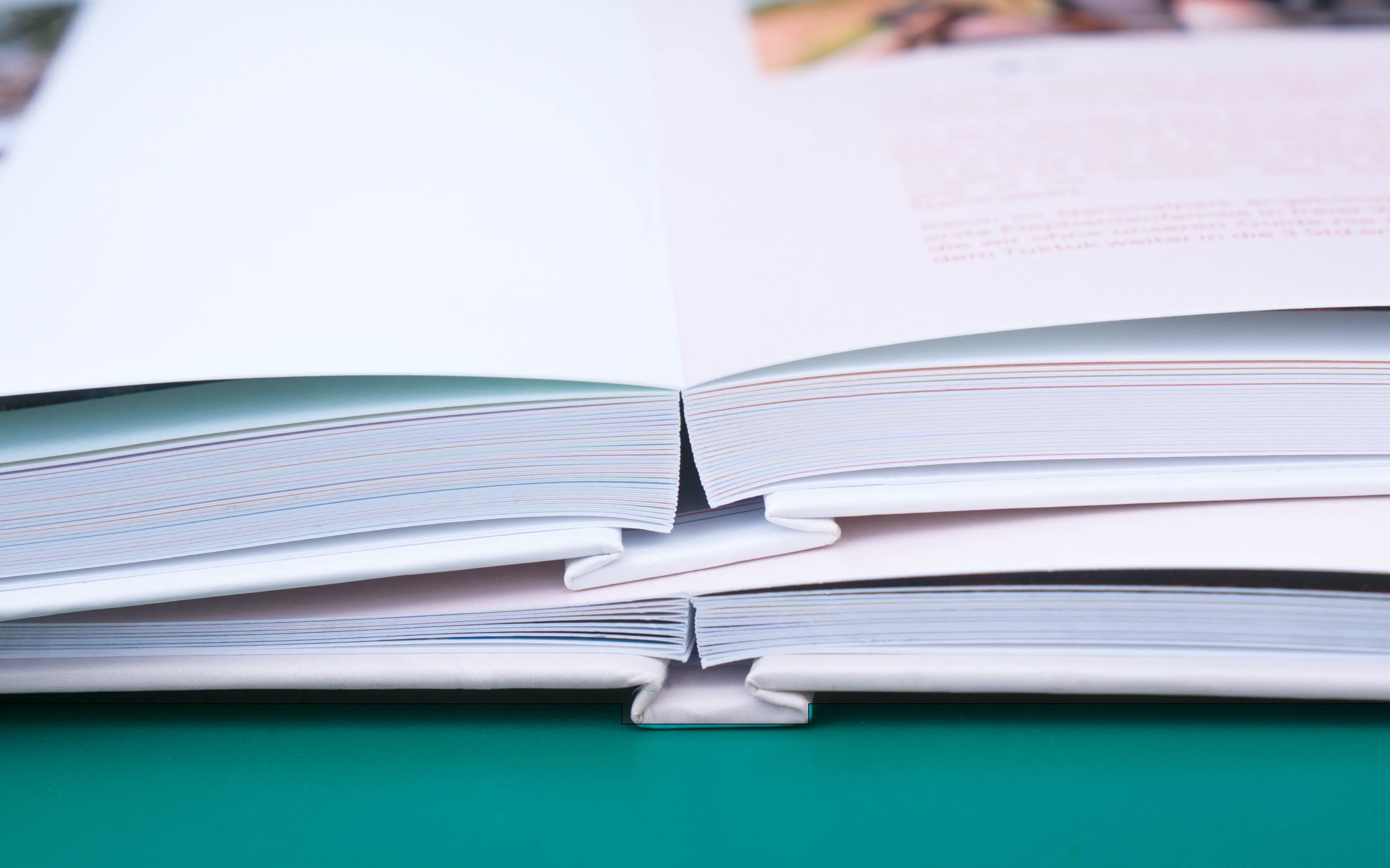 Close-up of two open photo books stacked on a green surface, focusing on the spines and pages.