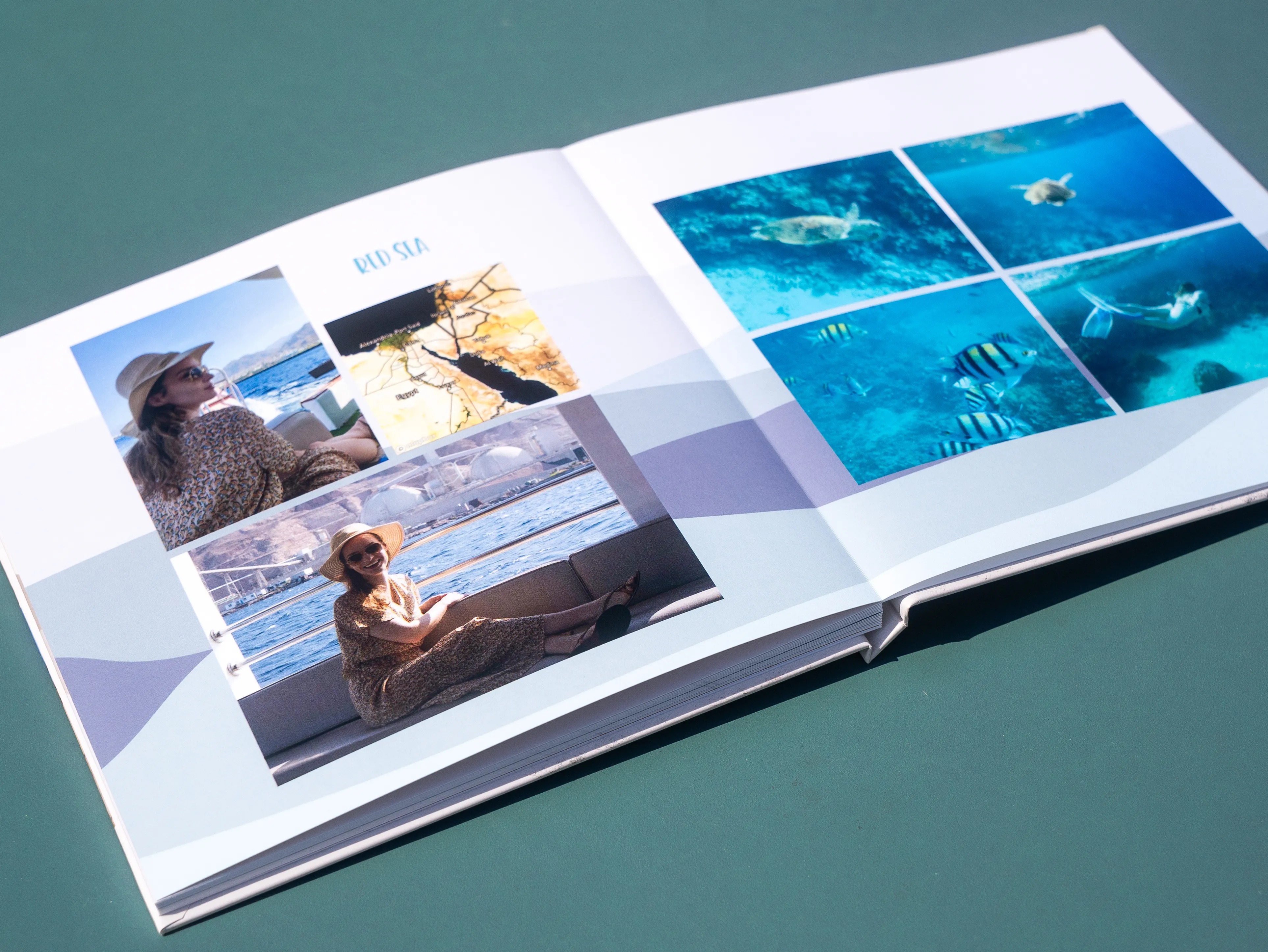 Open photo album on a table, featuring travel photos of a person on a boat and underwater scenes with fish and a turtle.