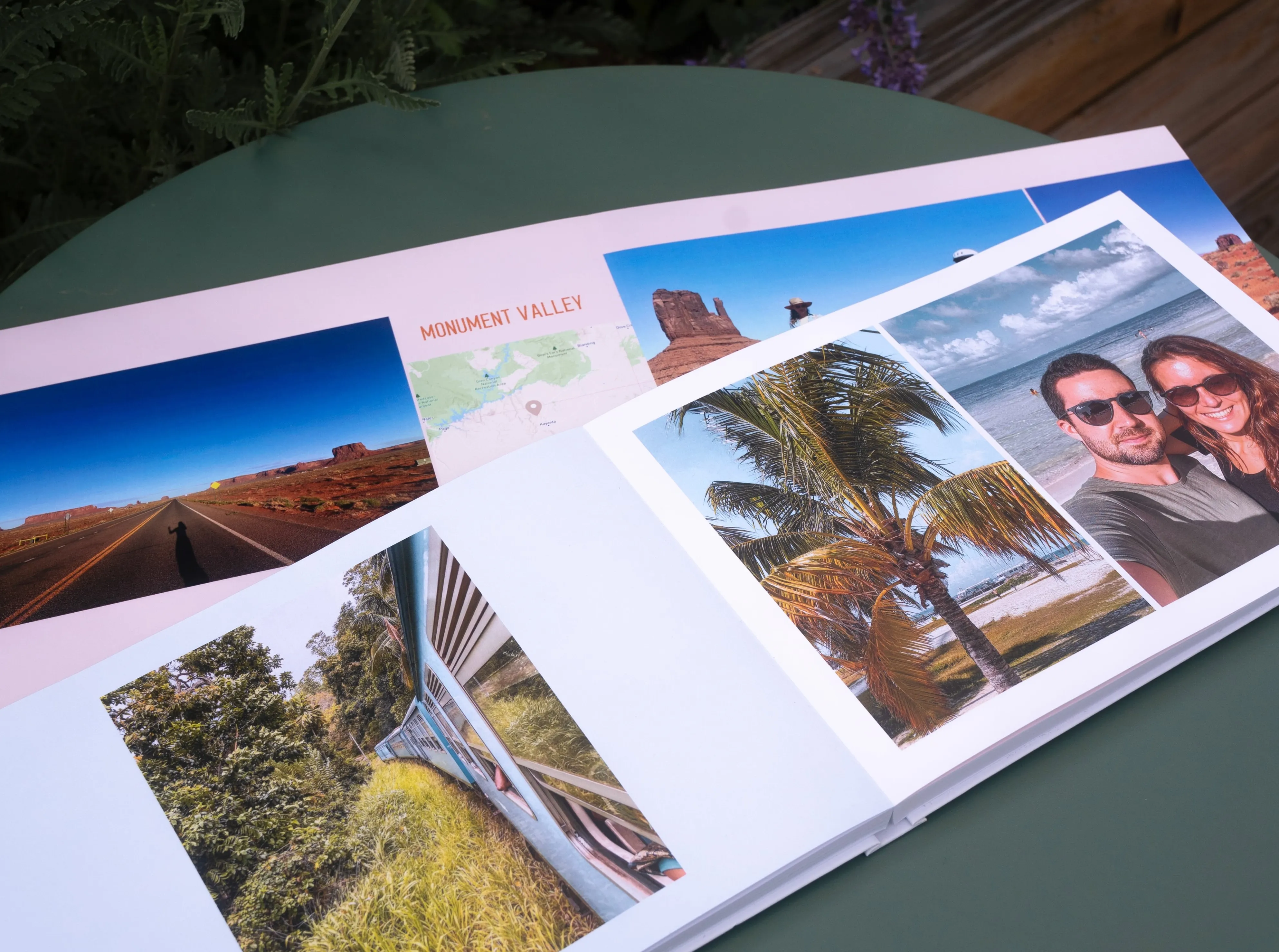 Open photo album on a table, showing travel photos of Monument Valley, palm trees, a couple, and scenic landscapes.