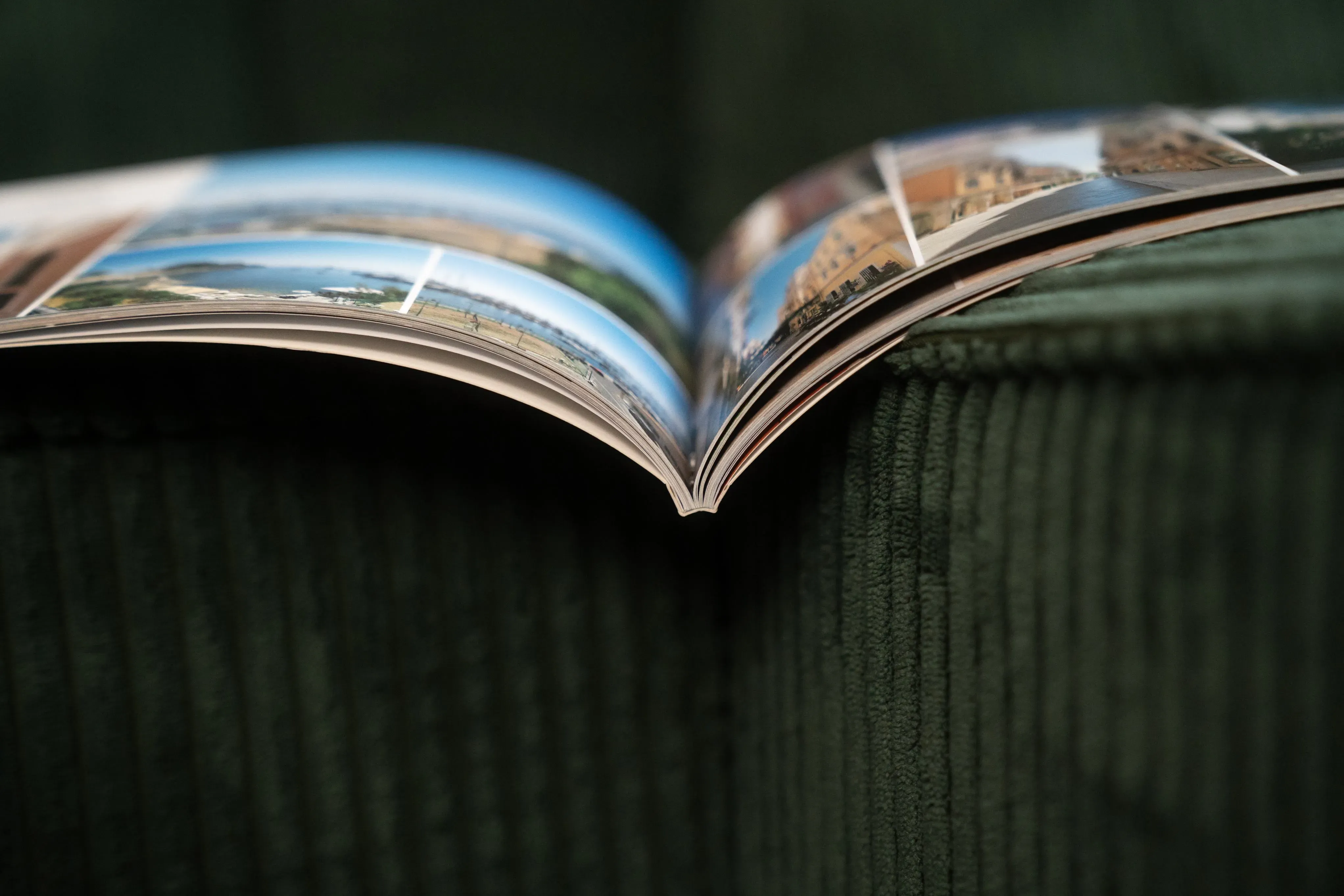 Open book with glossy pages displaying colorful images, resting on a dark green textured surface.