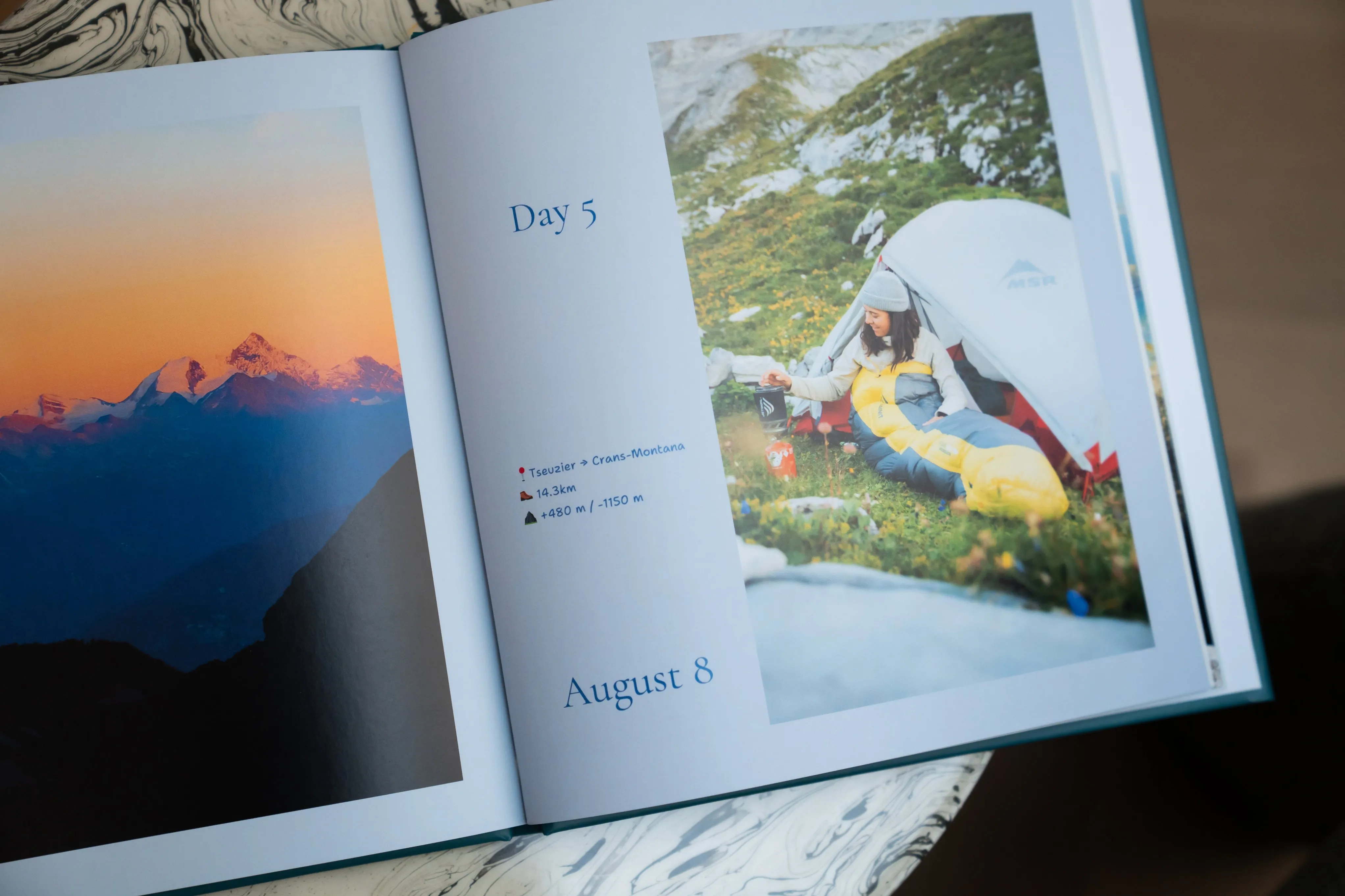 Ein aufgeschlagenes Urlaubsfotobuch, auf dessen linker Seite eine Berglandschaft und auf der rechten Seite ein Wohnmobil neben einem Zelt zu sehen ist, dazu Text über Wandern und Daten.