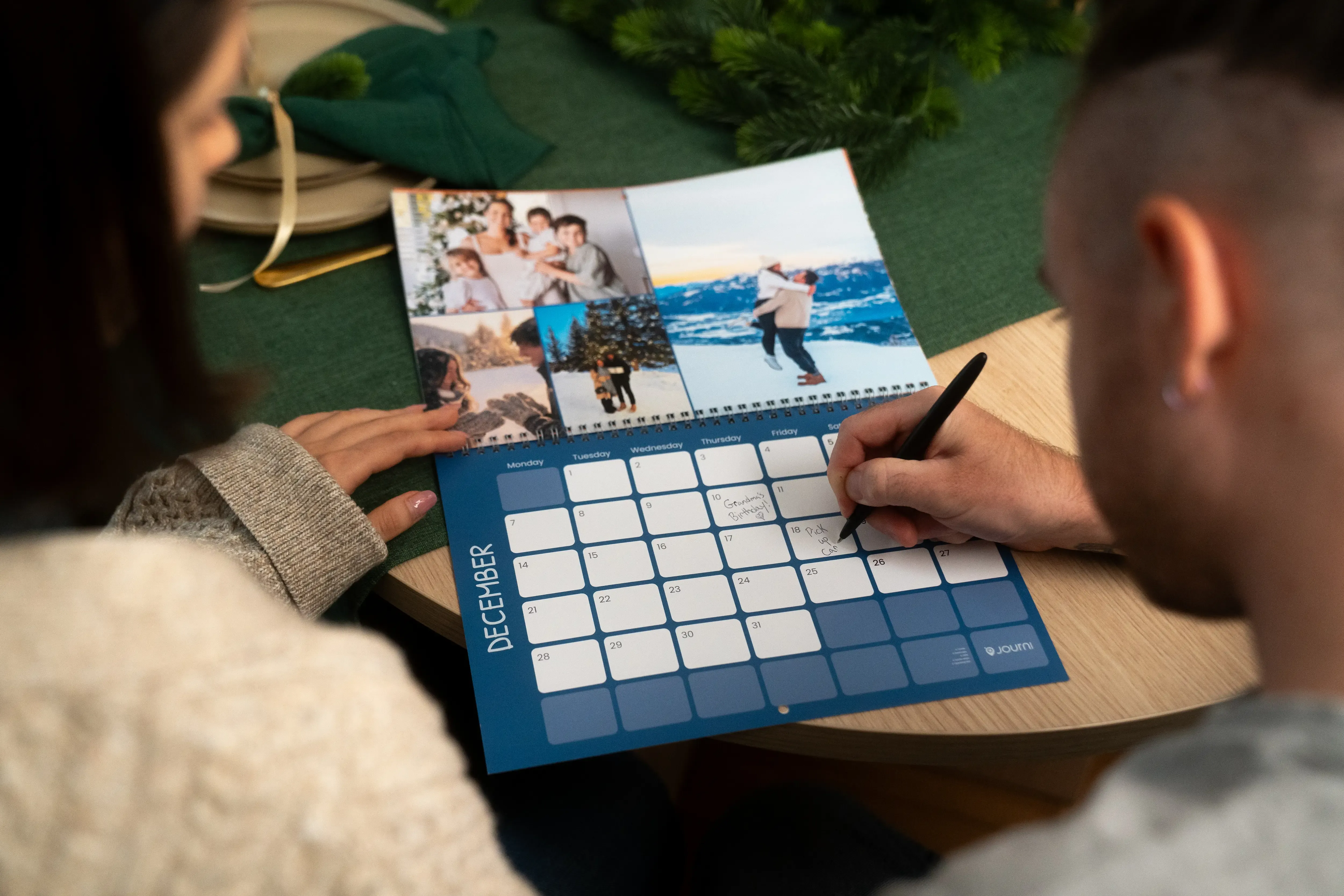 Two people planning on a December calendar featuring family photos, one writing with a pen.