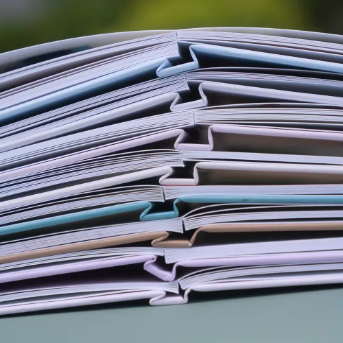 A stack of open layflat photo books with colorful pages, neatly arranged in a zigzag pattern, viewed from the side.
