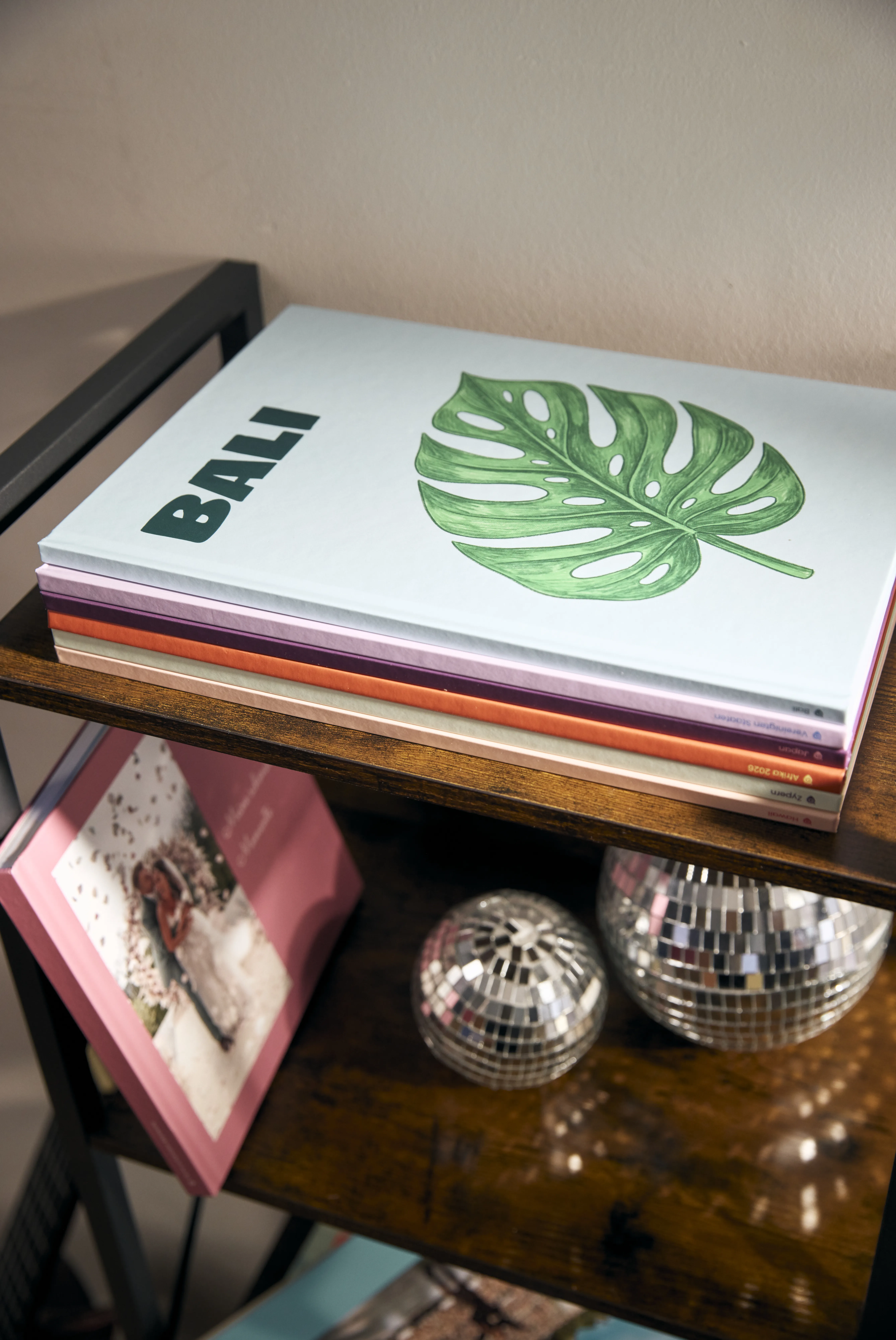 Ein Stapel bunter Reisefotobücher in einem Regal, darunter ein Hochzeitsalbum von Sarah Engels und Discokugeln als Deko.